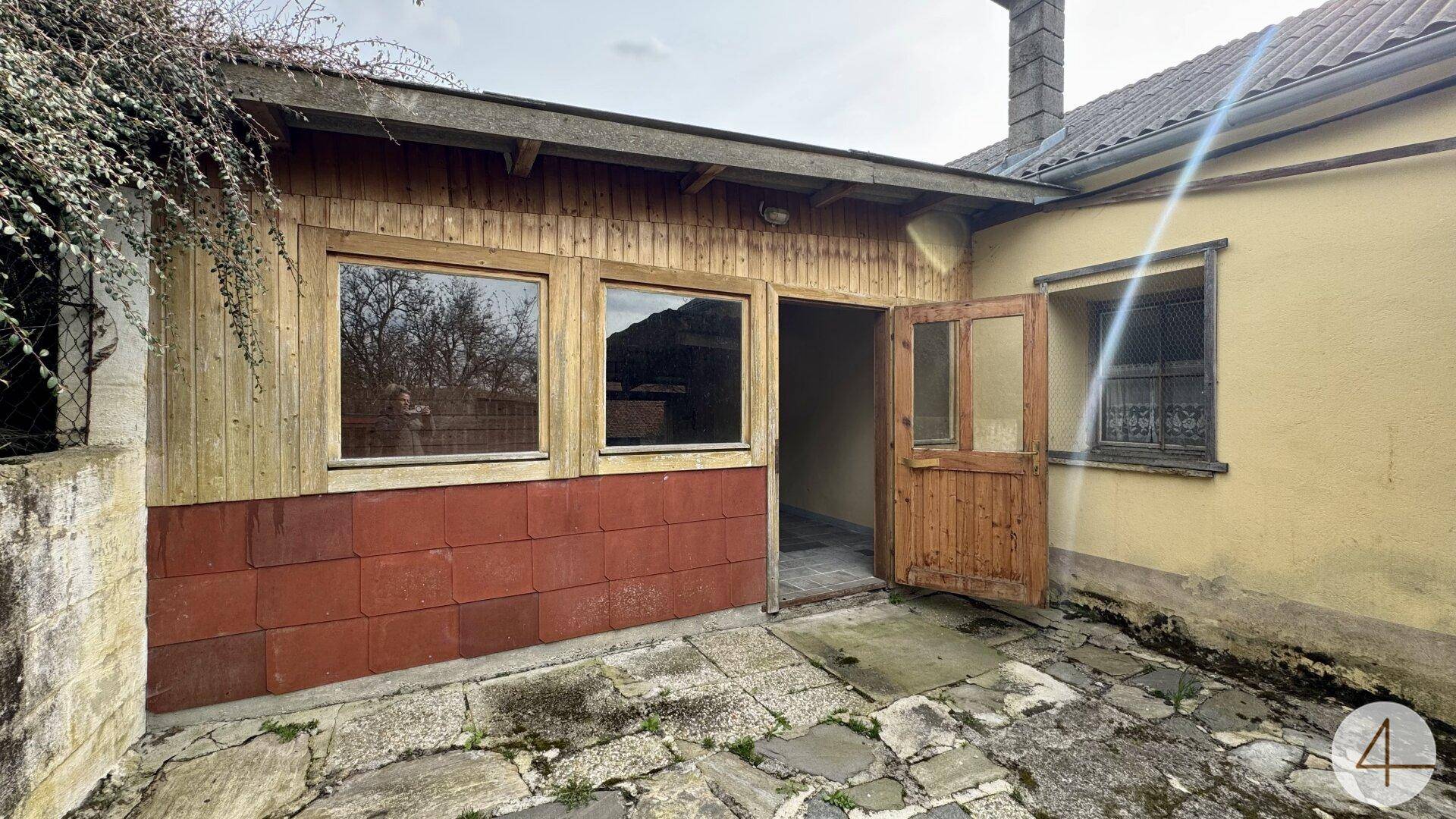 Kleines Nebengebäude mit Holzverkleidung und einem gepflasterten Bereich im Hinterhof.