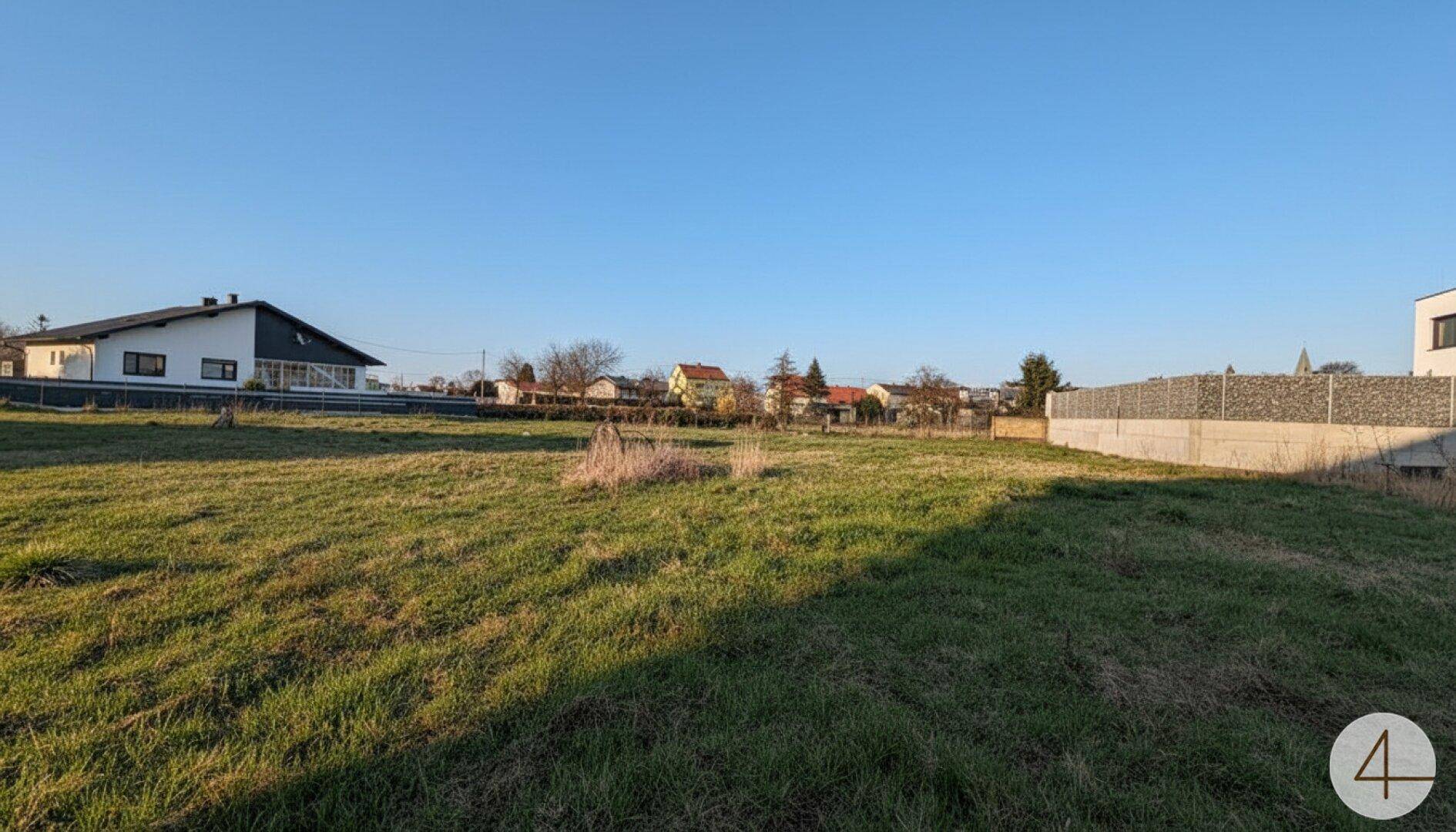 Weitläufiges unbebautes Grundstück mit angrenzender Bebauung und klarem Himmel.