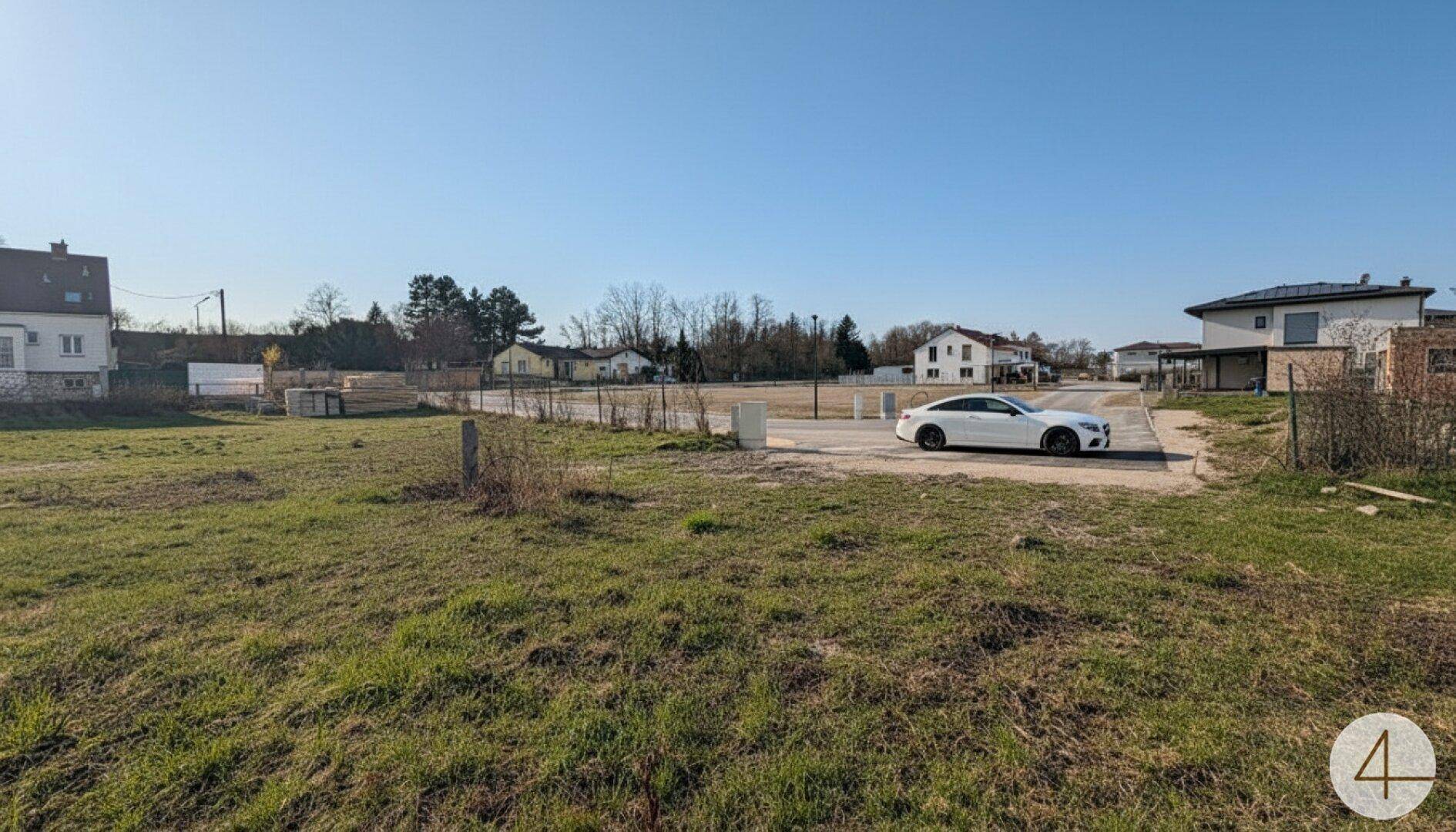 Offenes Grundstück mit gepflastertem Bereich und einem geparkten Auto in sonniger Umgebung.