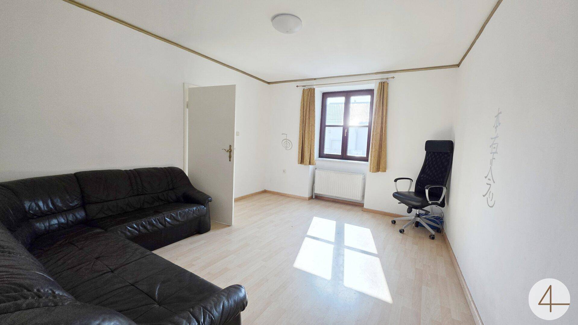 Wohnzimmer mit dunklem Sofa, hellem Boden und Fenster mit Vorhängen.