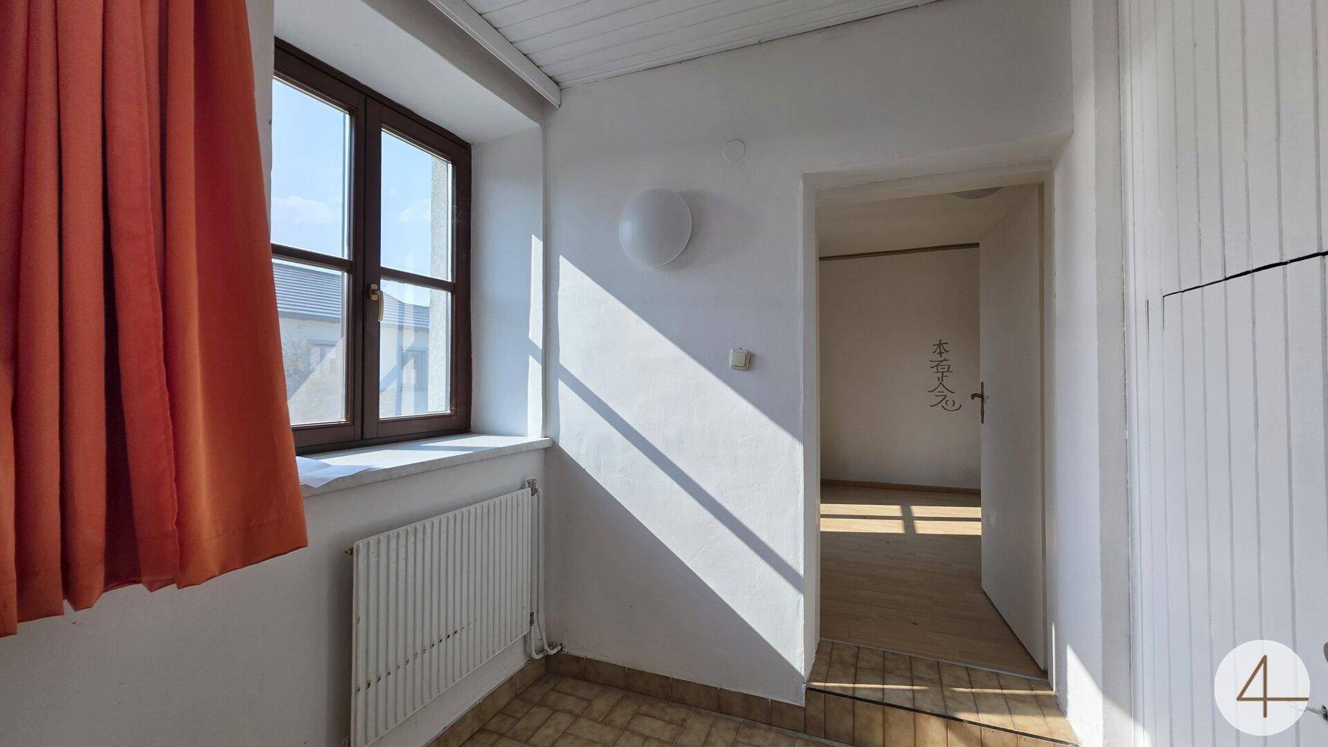 Heller Flur mit Holzfenster, Heizkörper und Zugang zu weiteren Räumen.