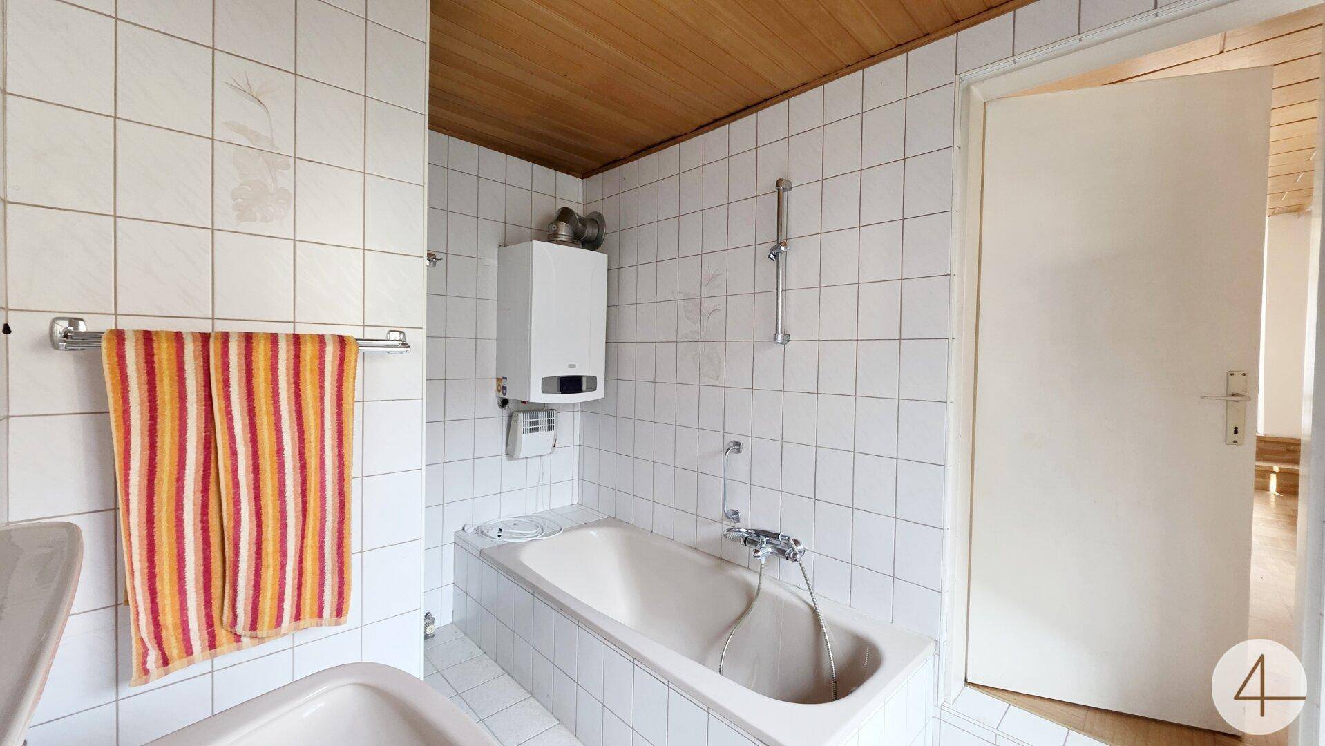 Badezimmer mit Badewanne, weißen Fliesen und Holzdecke.