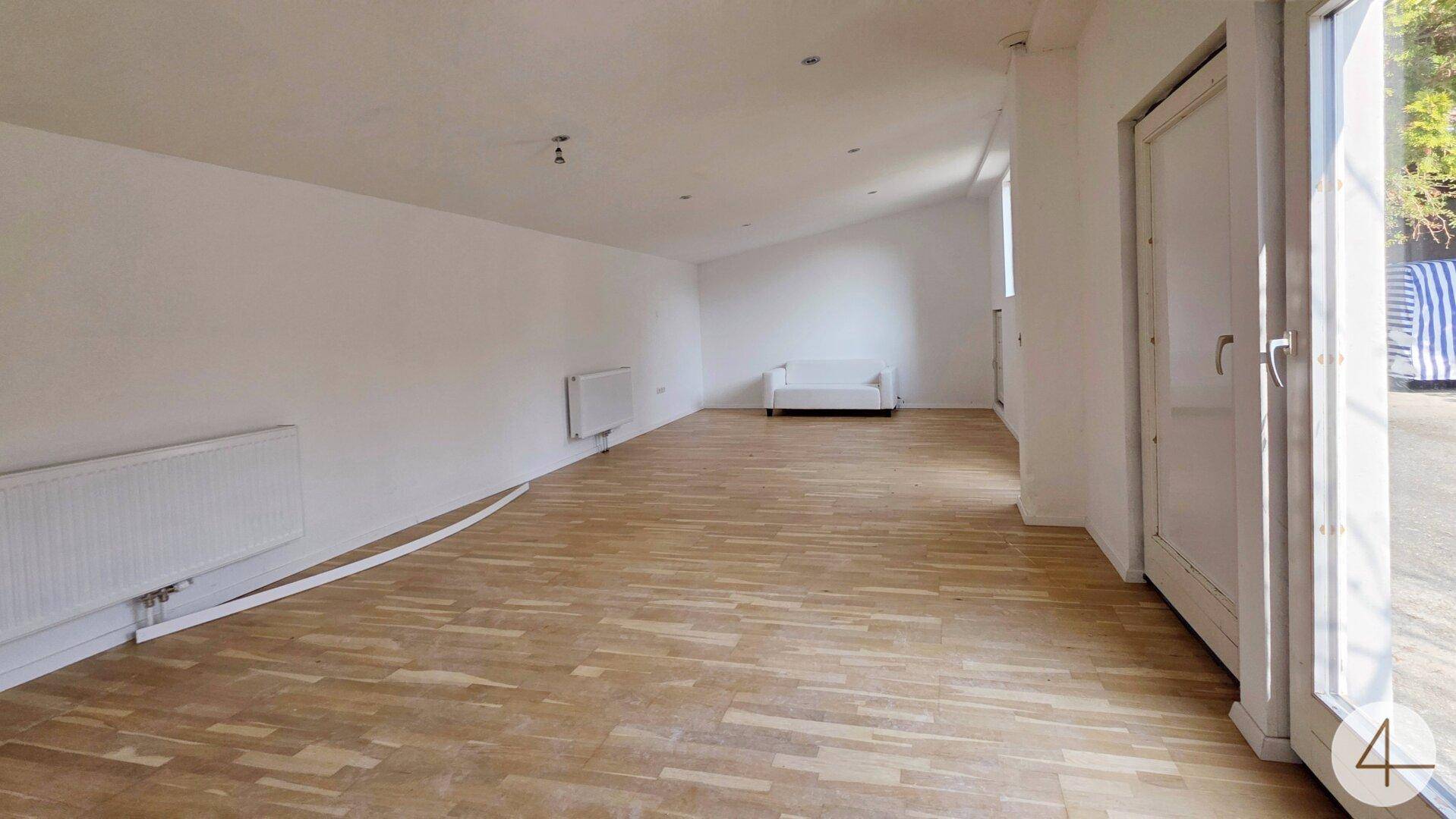 Großer, heller Raum mit Parkettboden, weißen Wänden und viel Tageslicht.