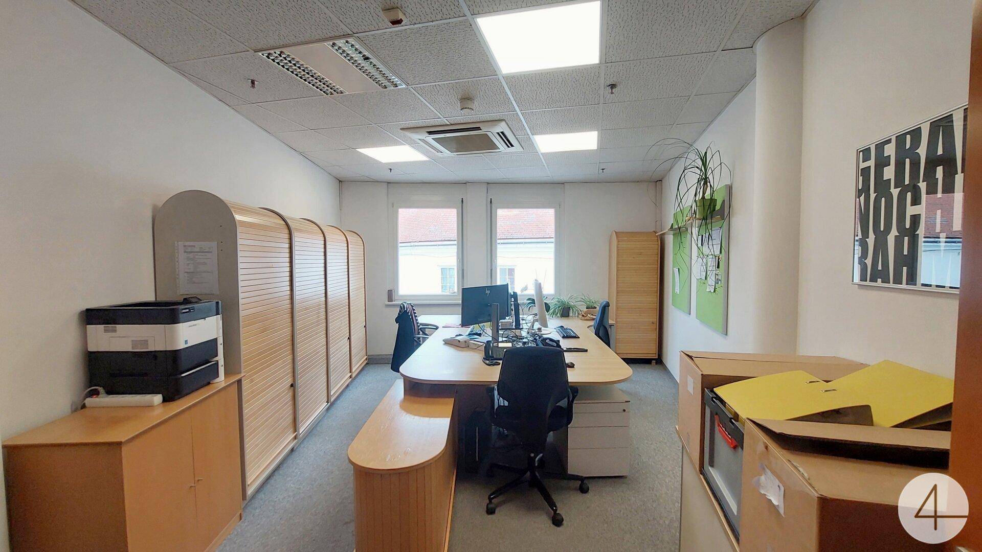 Modernes Büro mit mehreren Arbeitsplätzen, Teppichboden und großen Fenstern für natürliches Licht.