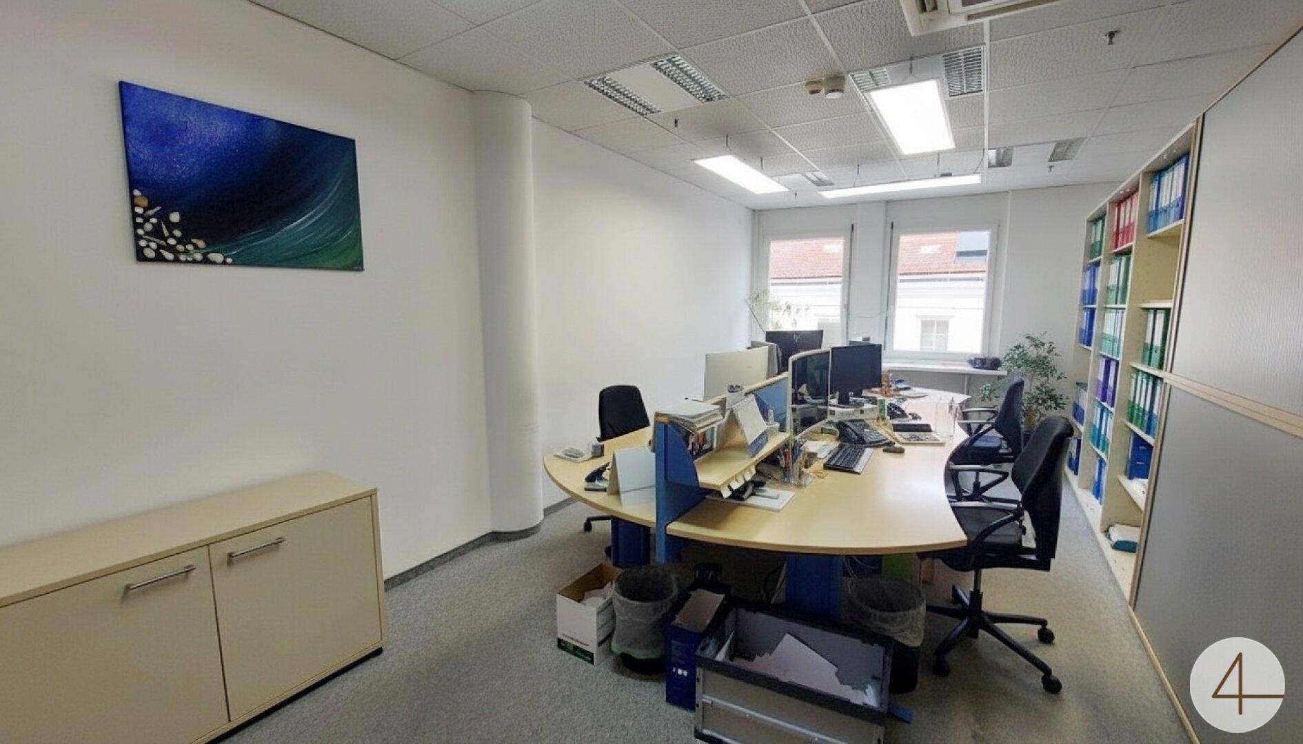 Großes Büro mit mehreren Arbeitsplätzen, Teppichboden und Regalen voller Aktenordner.