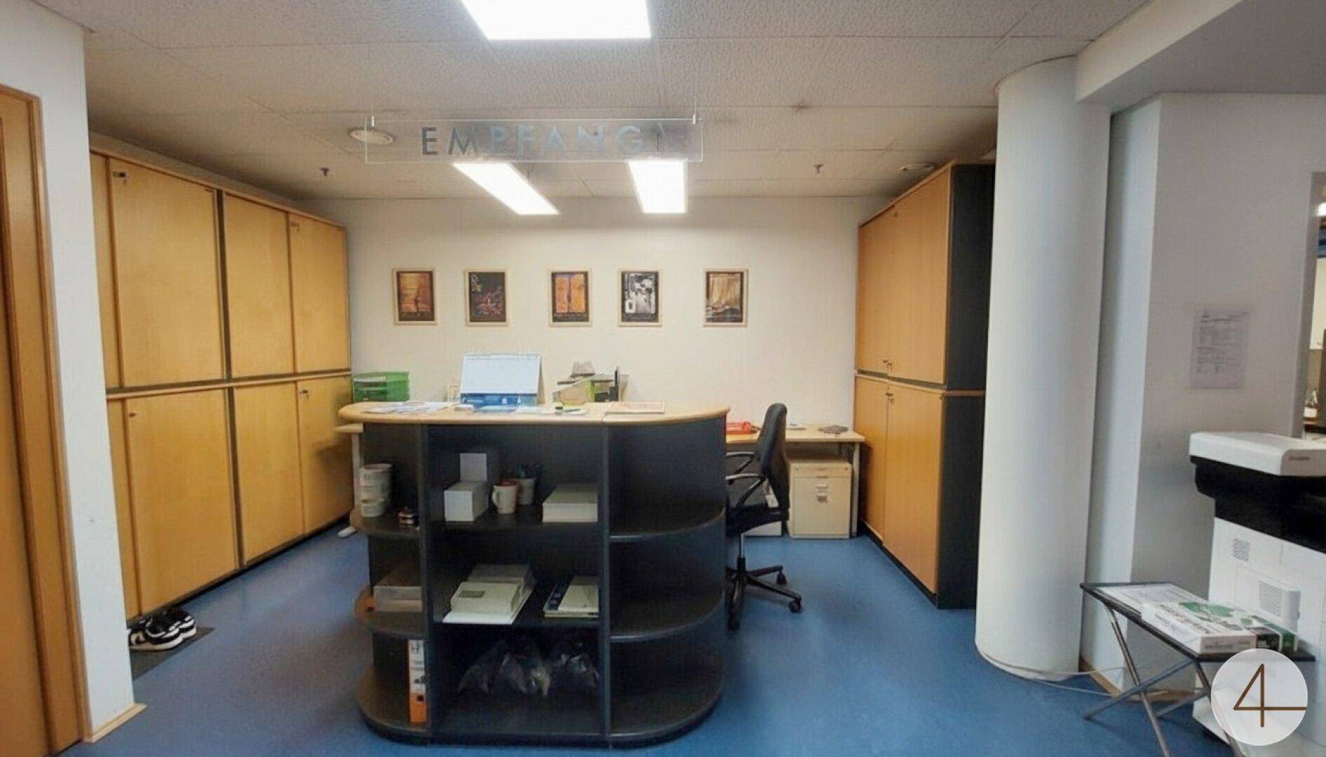 Heller Empfangsbereich mit einem runden Schreibtisch, Büromöbeln und Bildern an der Wand.