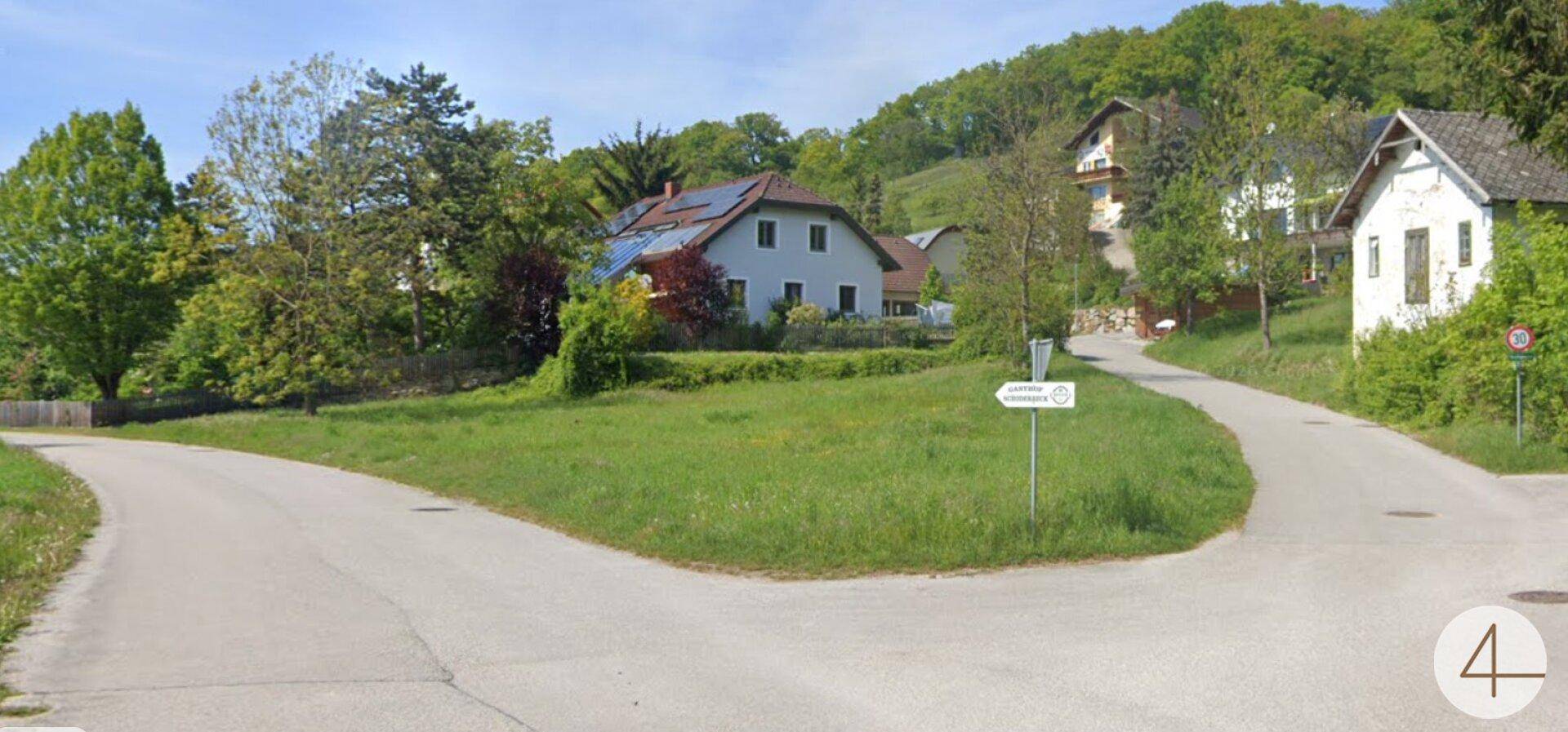 Weitläufige Ansicht eines Grundstücks an einer Straßenkreuzung mit Häusern und viel Grün.