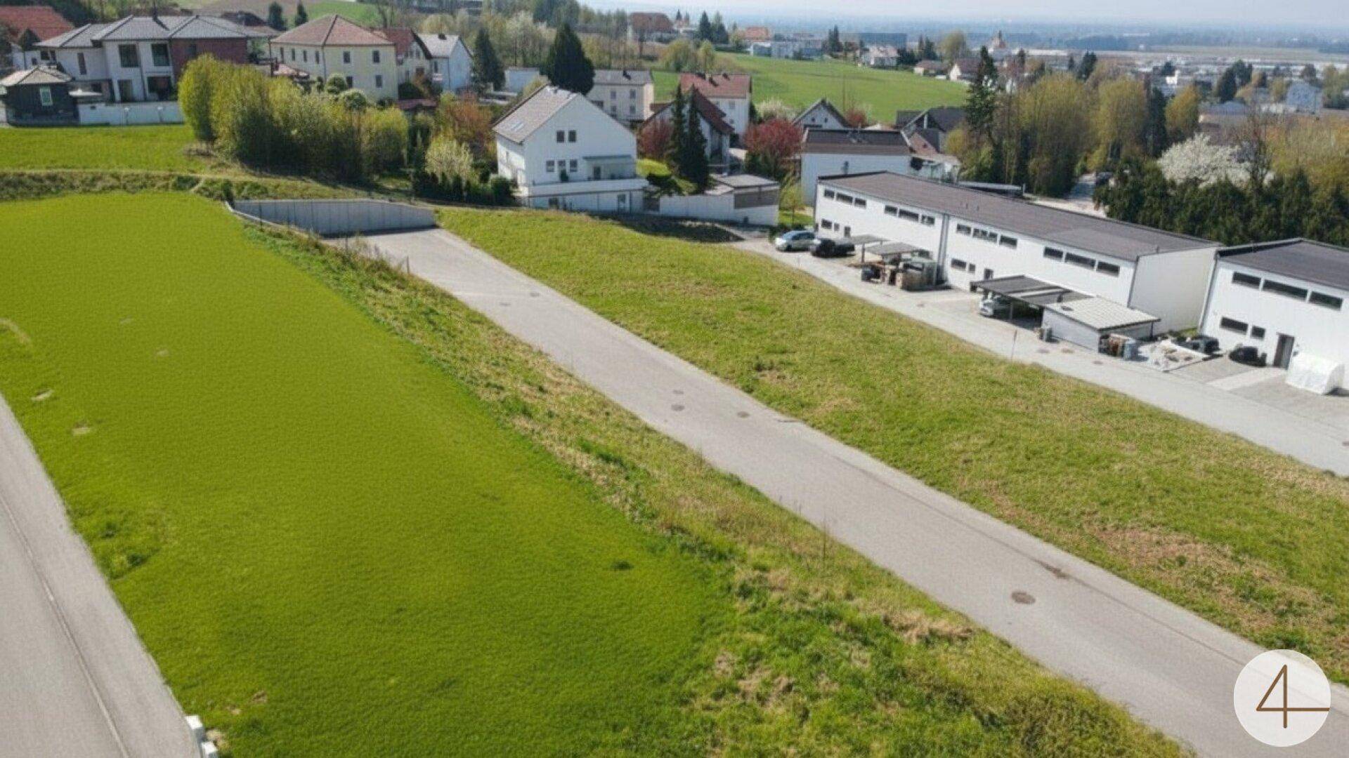 Luftaufnahme eines unbebauten Grundstücks mit angrenzenden Gebäuden und ländlicher Umgebung.