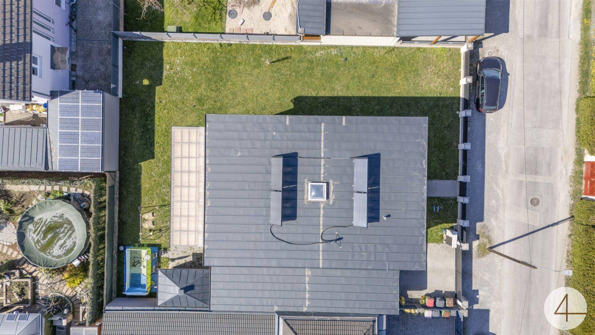 Draufsicht auf das Flachdach des Hauses mit Solarpaneelen und Dachfenster.
