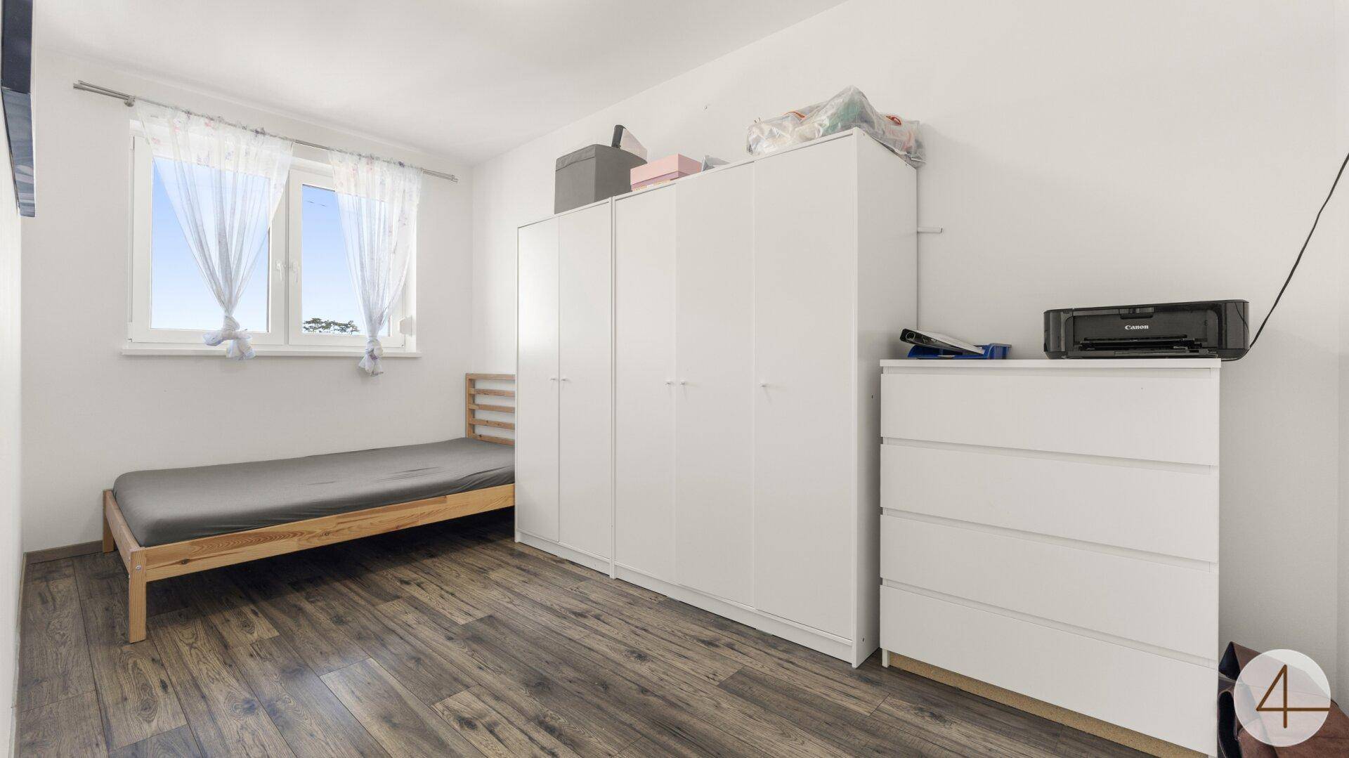 Helles Schlafzimmer mit Einzelbett, weißem Kleiderschrank und Holzboden.