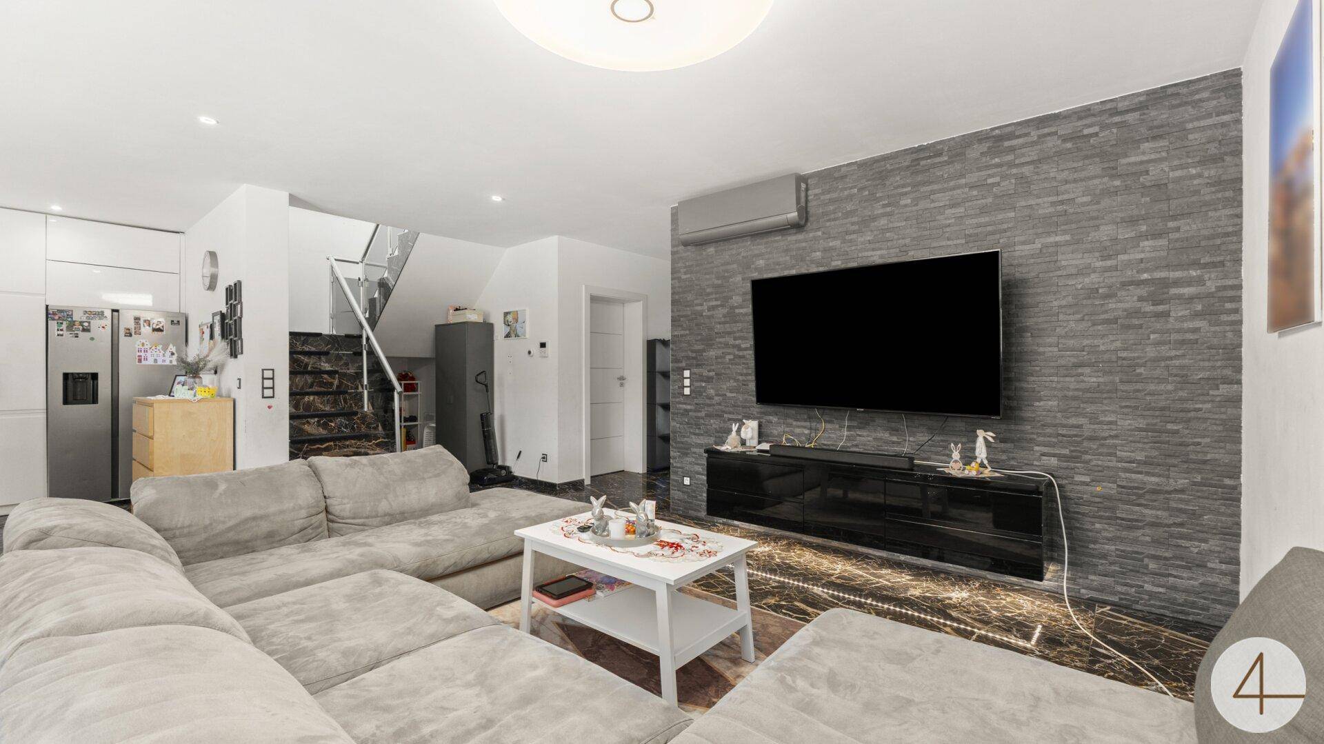 Wohnbereich mit großem Ecksofa, TV-Wand und Treppe zum Obergeschoss.