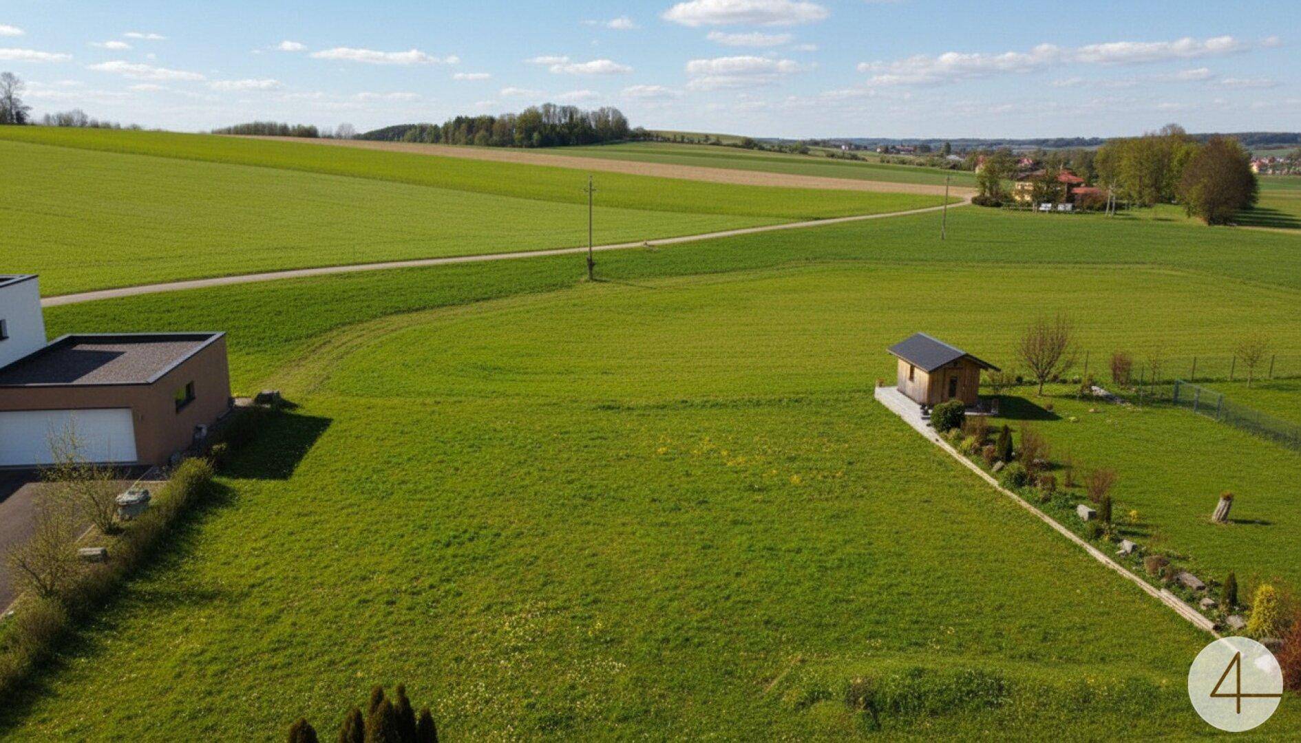 Luftaufnahme eines Anwesens mit Haus, Garage und kleinem Gartenhaus, umgeben von weiten grünen Feldern.