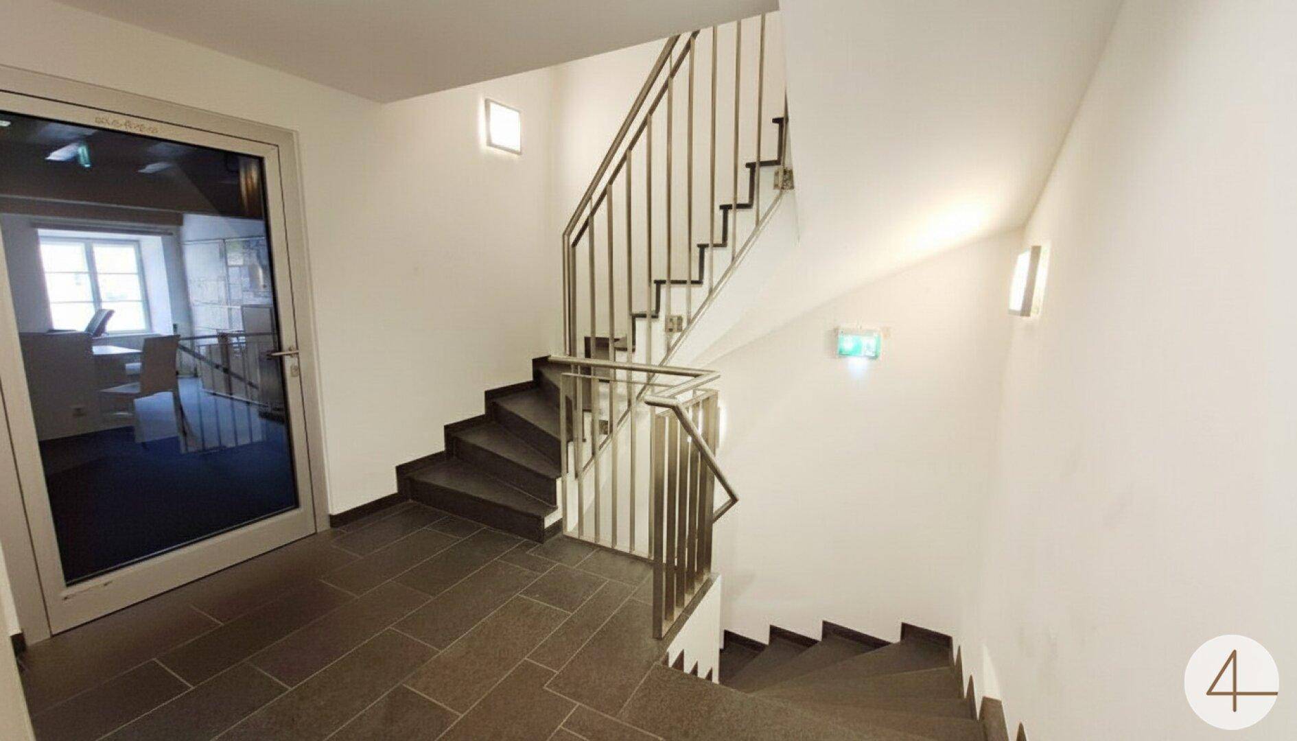 Modernes Treppenhaus mit dunklen Fliesen, Edelstahlgeländer und weiß gestrichenen Wänden.