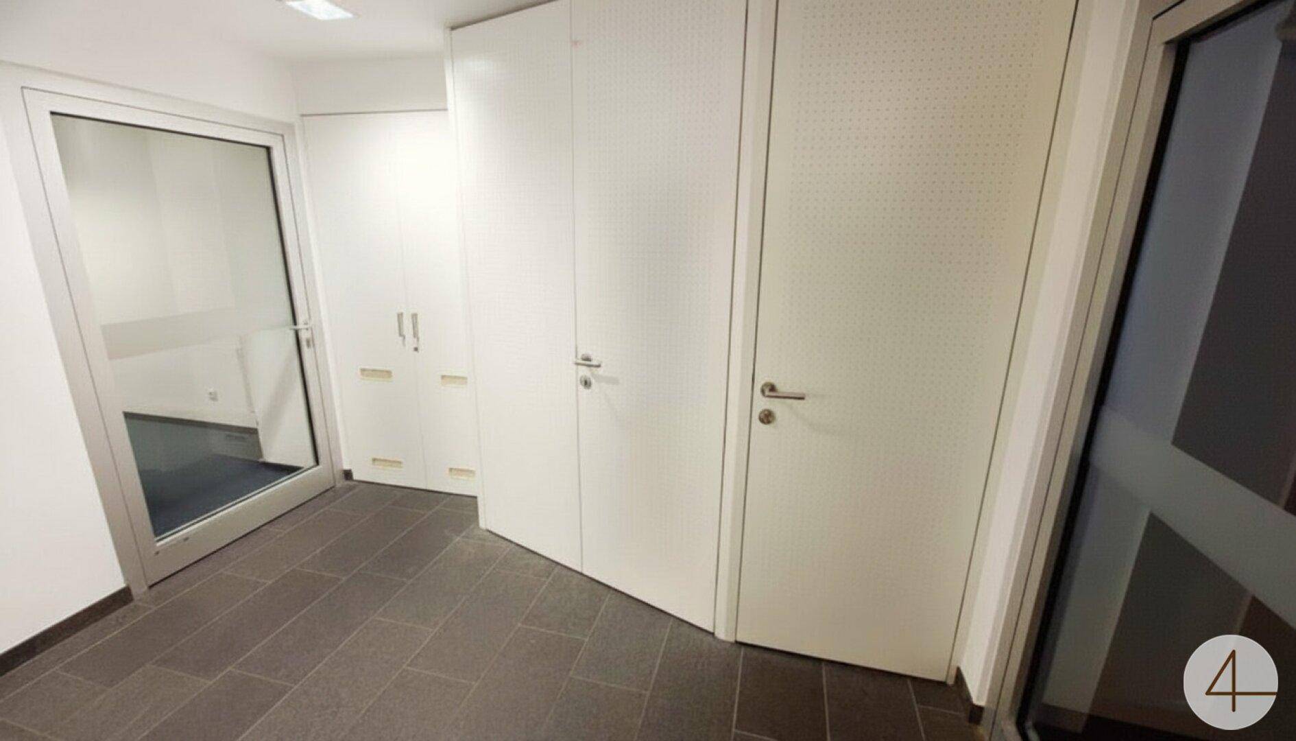 Heller Flur mit dunklen Fliesen, weißen Türen und einer Glastür, die zu einem weiteren Raum führt.