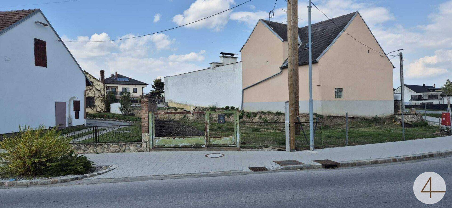 Blick auf die Straße mit Bürgersteig, Zaun und umliegenden Häusern in ländlicher Umgebung.