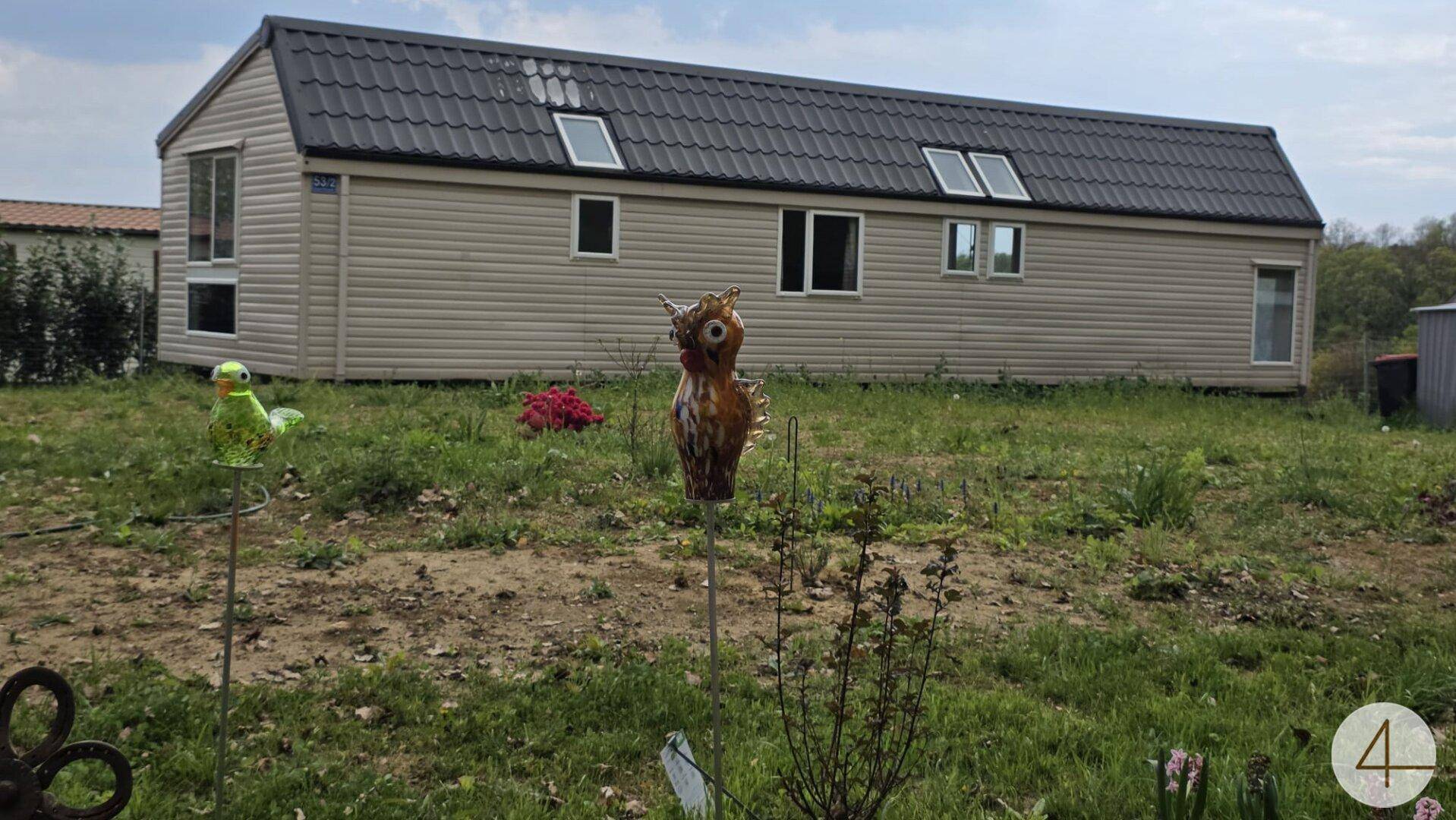 Rückseite des Mobilheims mit Dachfenstern und einem Gartenbereich mit dekorativen Elementen.