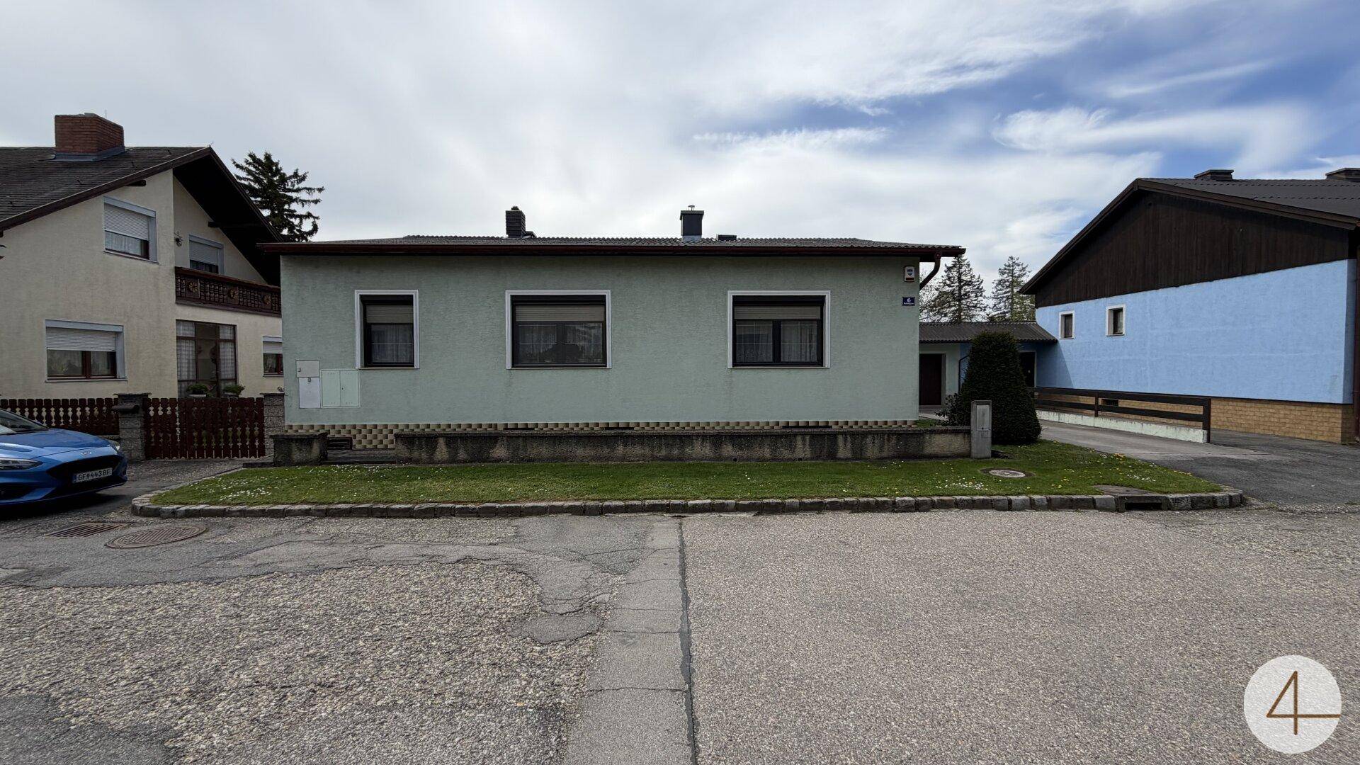 Vorderansicht des Hauses von der Straße aus mit einer schlichten Fassade und kleinen Fenstern.