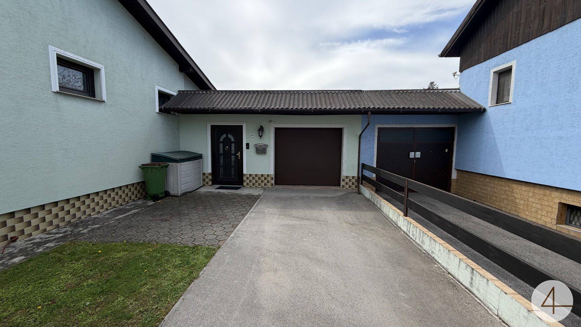 Eingangsbereich mit Garage, Einfahrt und einer Rampe, die zu einem weiteren Gebäudeteil führt.