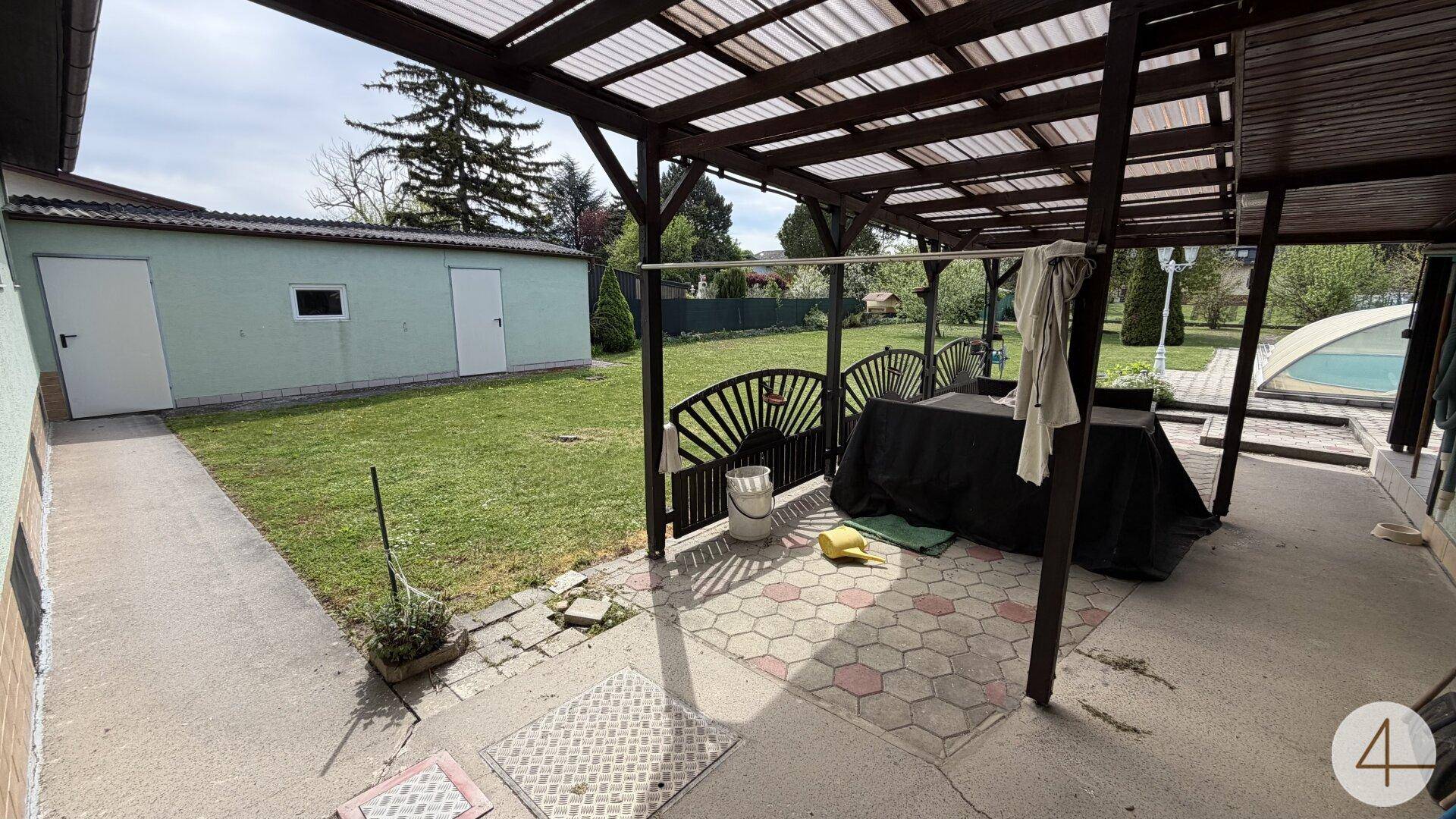 Überdachte Terrasse mit Sitzgelegenheiten und Blick auf den Garten mit Schuppen und Pool.