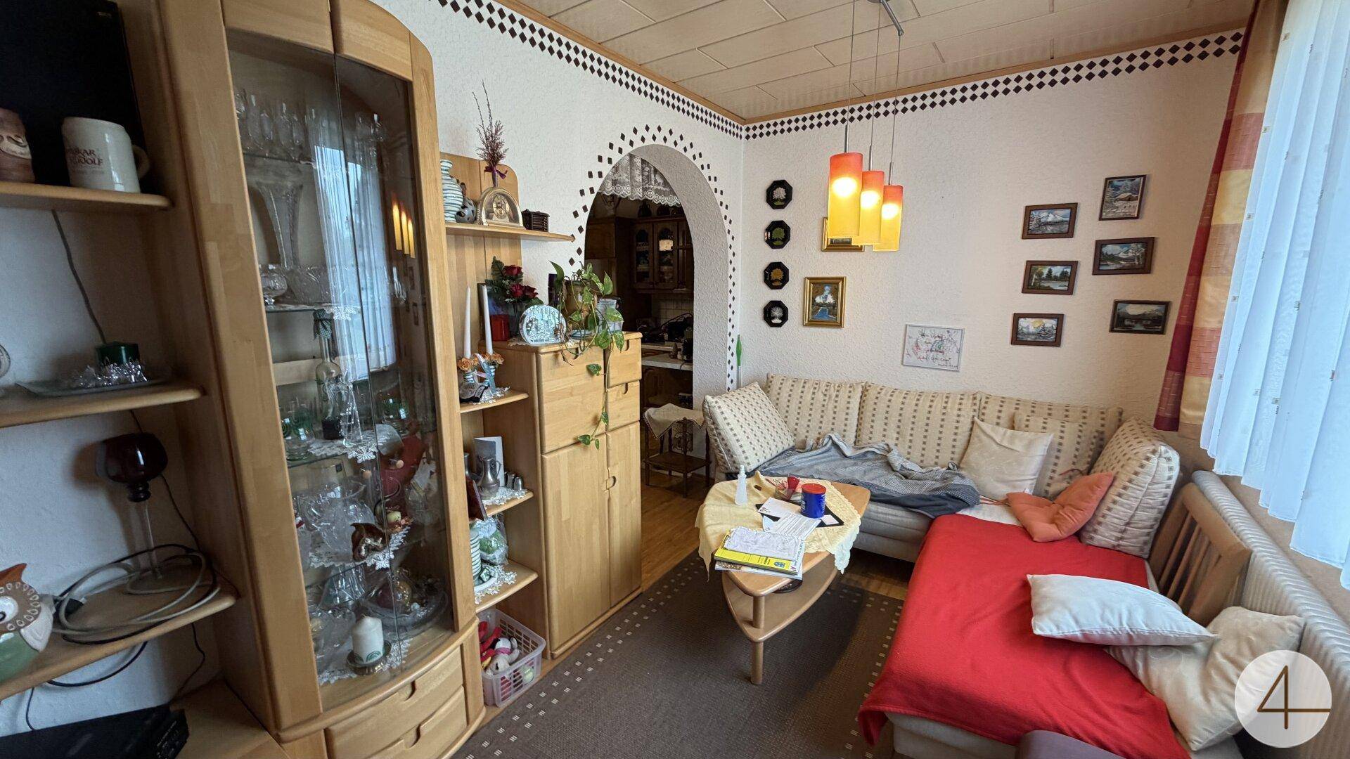 Kleiner, gemütlicher Wohnbereich mit Sofa, Holzelementen und einem Durchgang zur Küche.