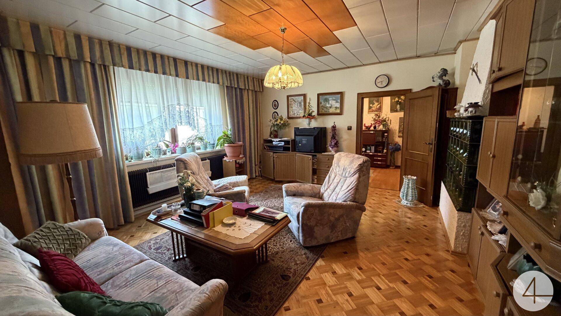 Gemütliches Wohnzimmer im traditionellen Stil mit Parkettboden, Kachelofen und Blick in den Flur.