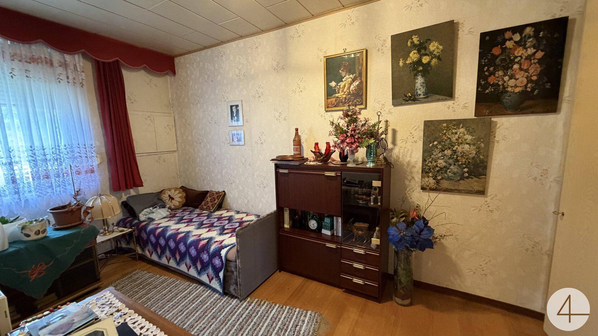 Schlafzimmer mit Einzelbett, Holzfußboden und floraler Tapete, dekoriert mit Bildern.