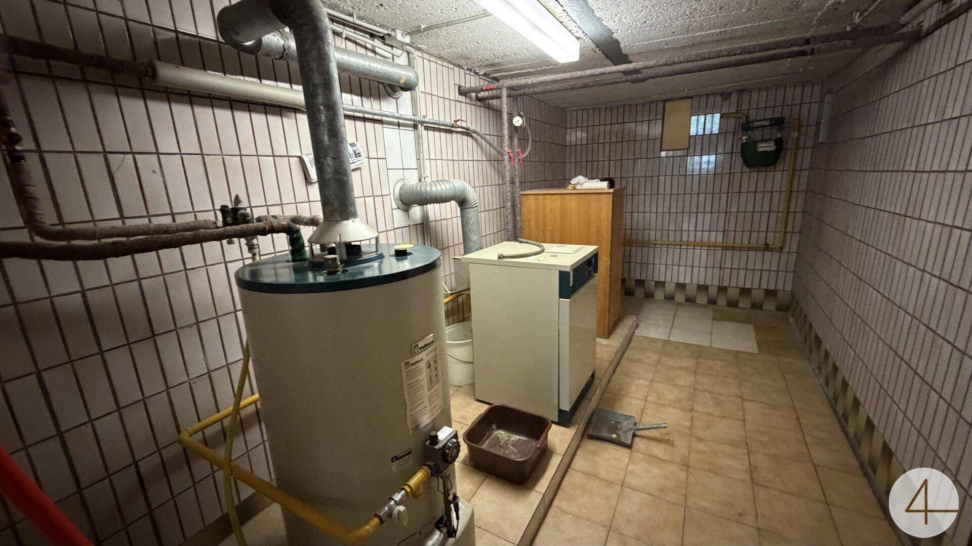 Heizungsraum im Keller mit Boiler, Heizungsanlage und sichtbaren Rohren an den Wänden.