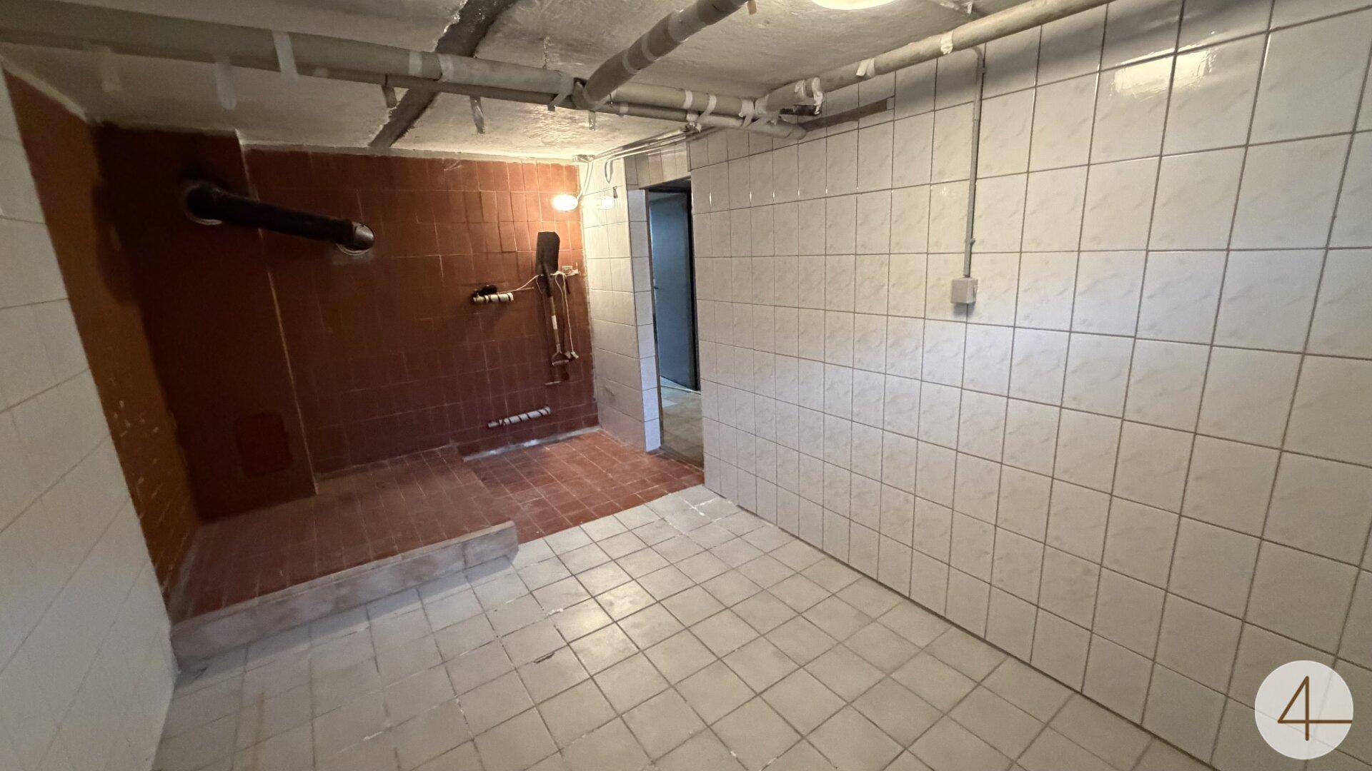 Funktionaler Kellerraum mit gefliesten Wänden und Boden sowie einer einfachen Duschgelegenheit.