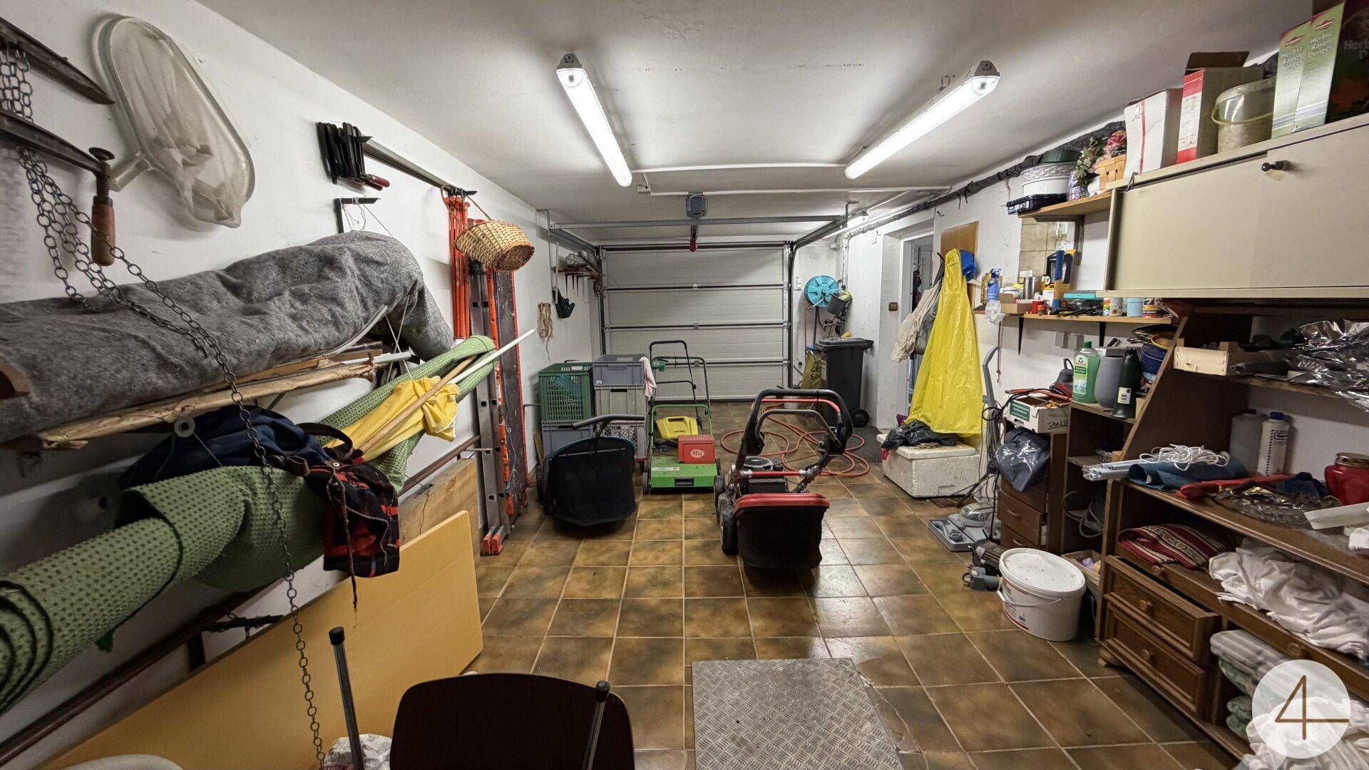 Geräumige Garage mit Fliesenboden, Stauraum und verschiedenen Gartengeräten.