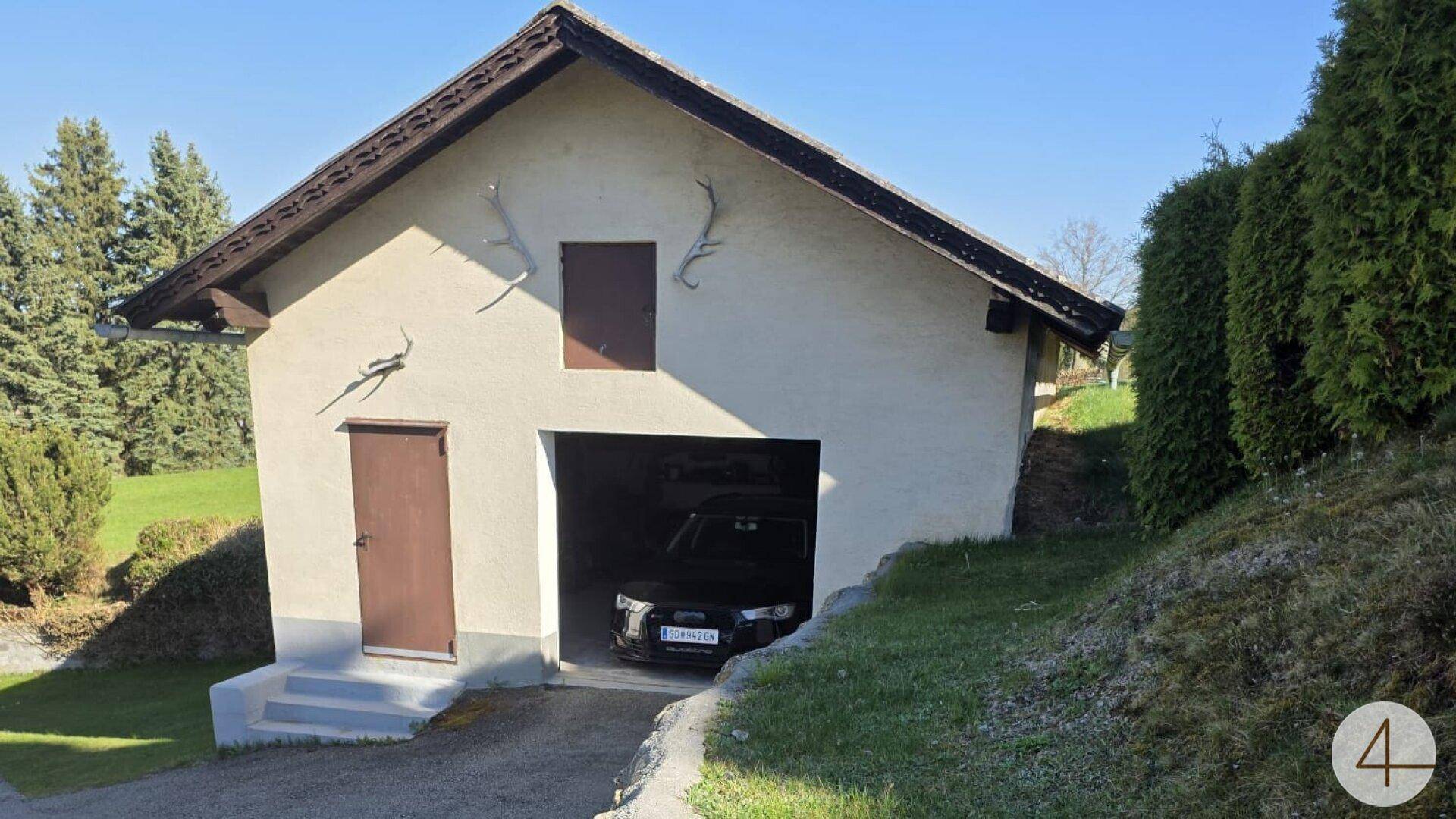 Gebäude mit integrierter Garage und einem geparkten Auto, verziert mit Hirschgeweihen an der Fassade.