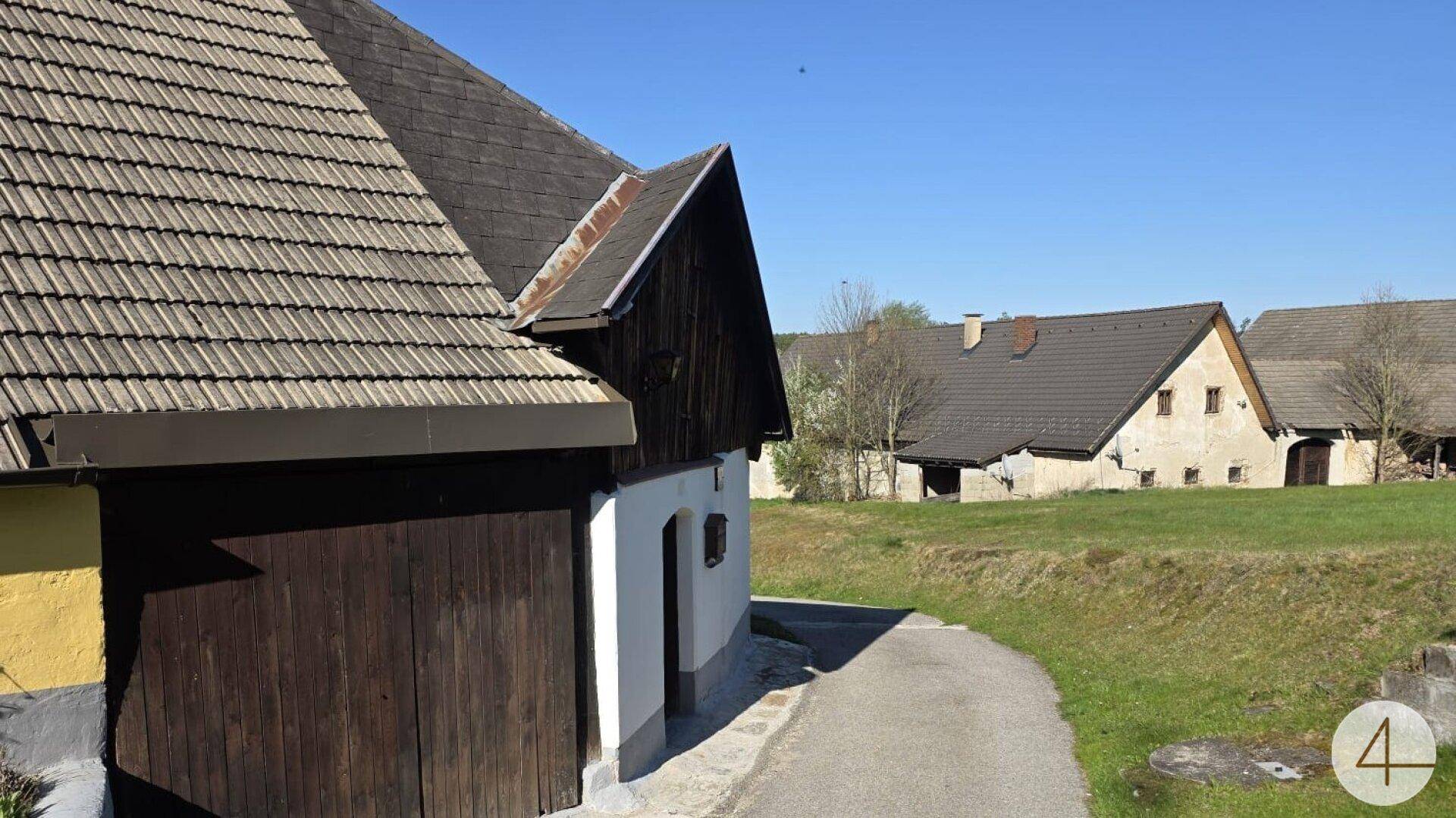Gebäude mit dunklem Ziegeldach und Holzelementen neben einem gepflasterten Weg in ländlicher Umgebung.