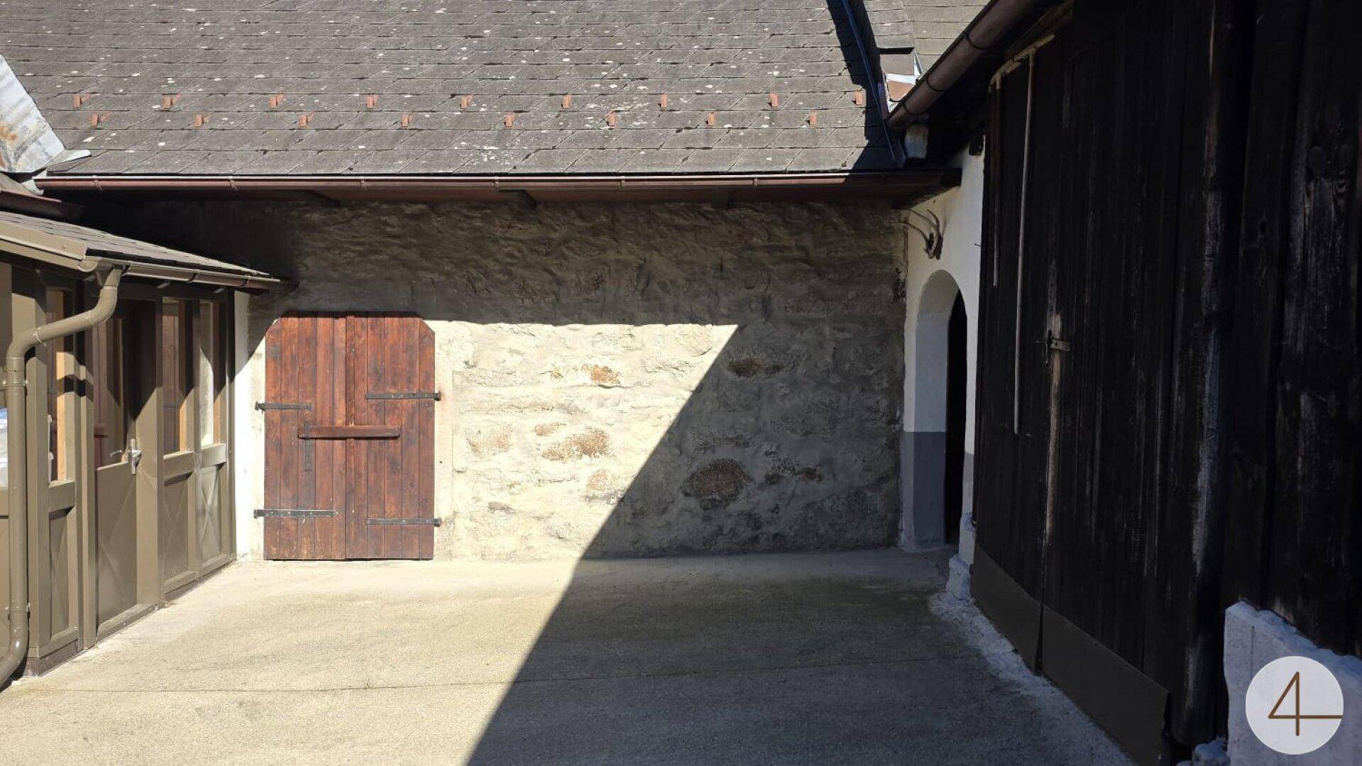 Rustikale Steinwand mit einer Holztür und einem gepflasterten Bereich im Sonnenlicht.