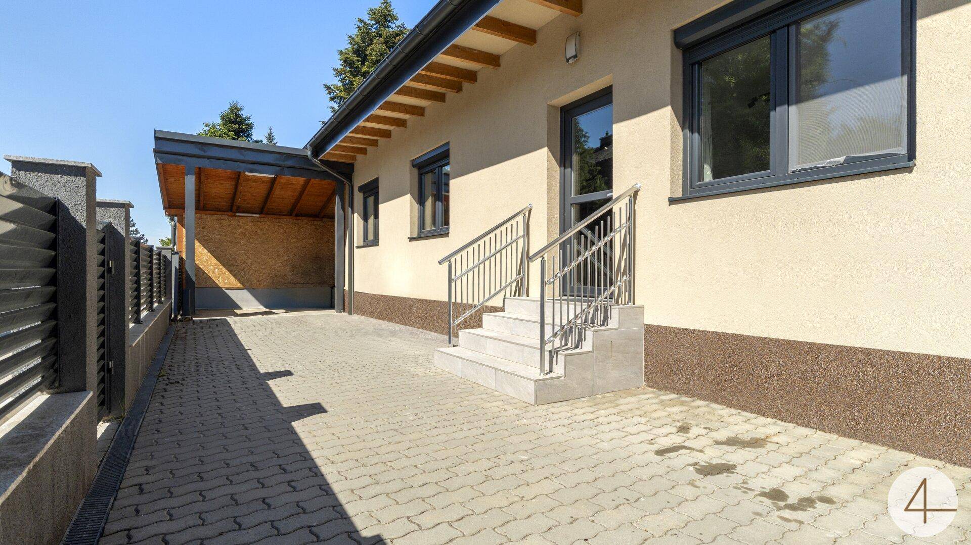 Seitenansicht des Hauses mit Eingangstreppe, gepflasterter Zufahrt und Carport.