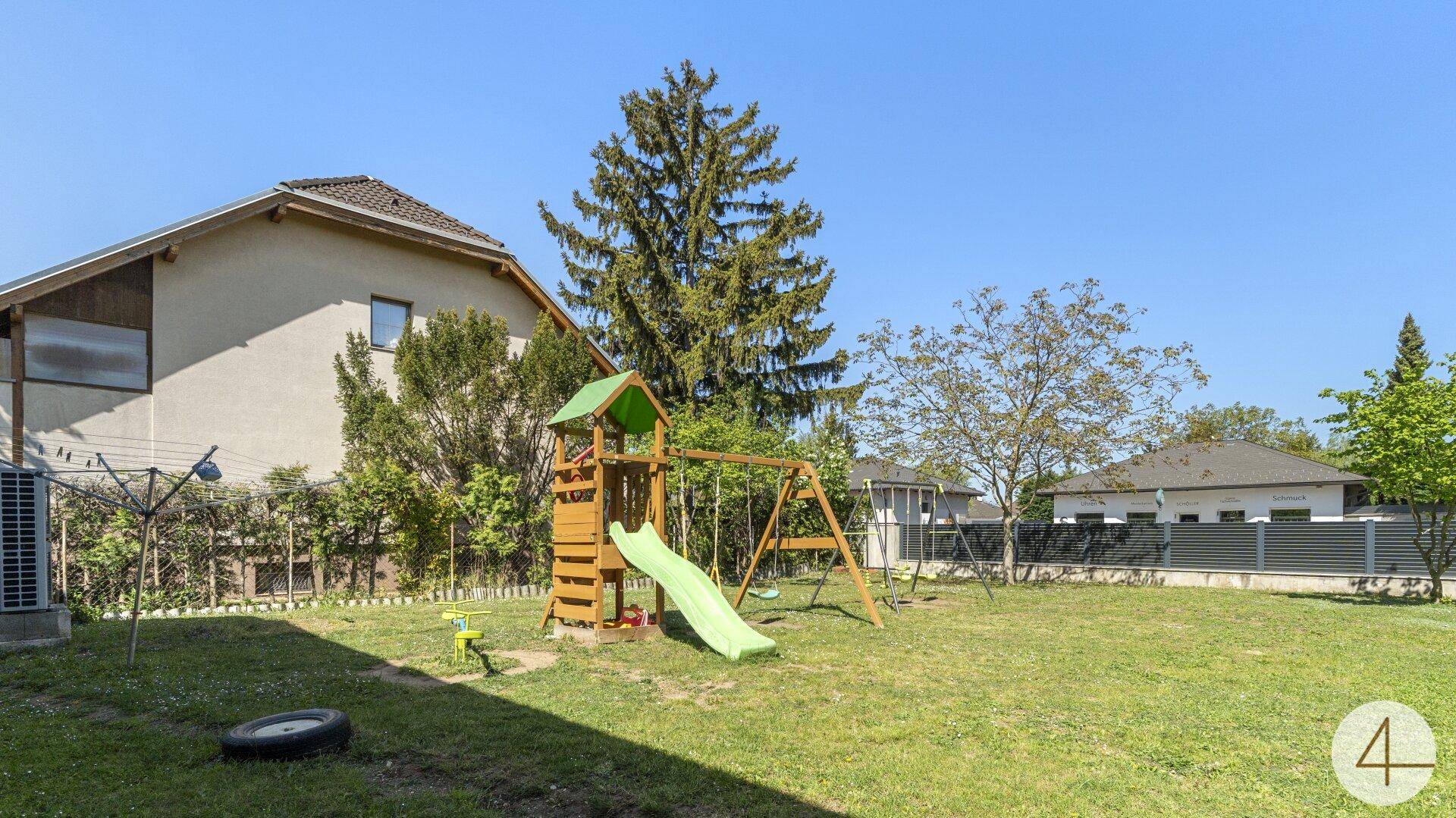 Großer Gartenbereich mit Spielplatz, Rutsche, Schaukeln und gepflegtem Rasen.