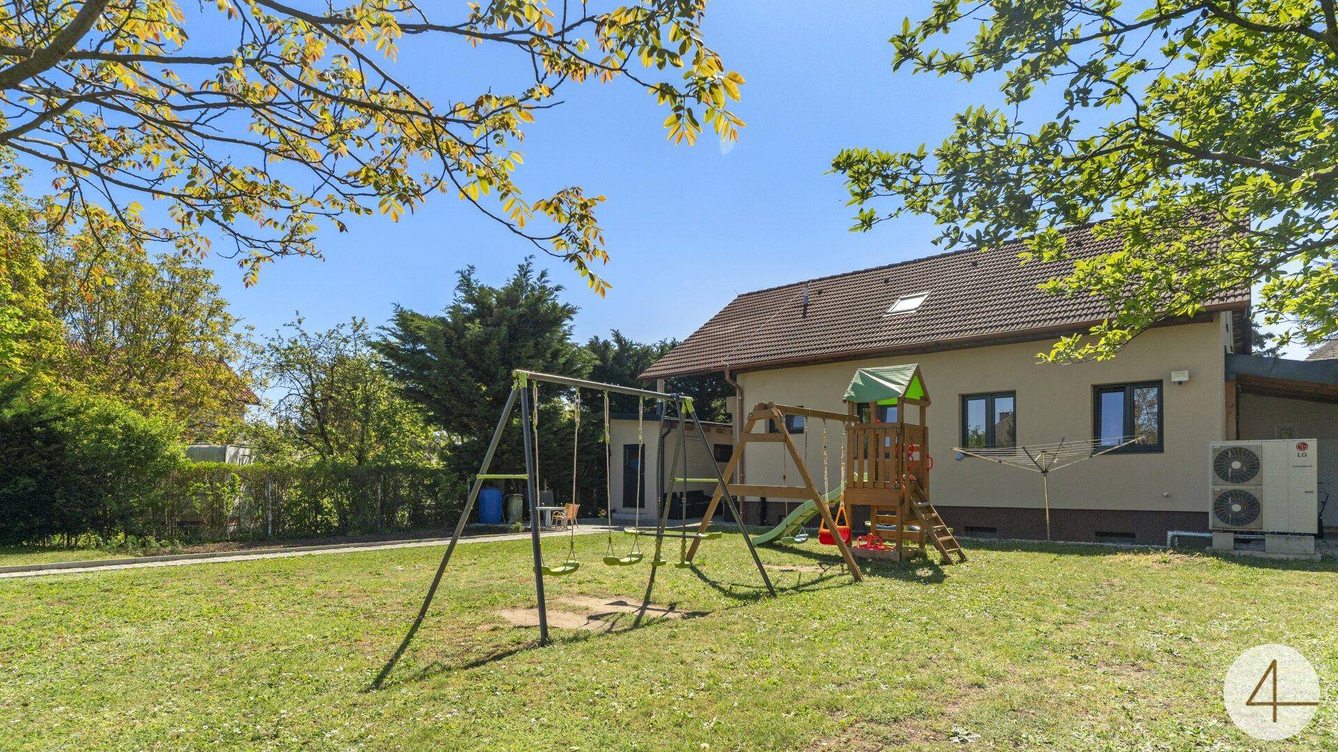Weitläufiger Garten mit Kinderspielplatz, Rasenfläche und Blick auf die Hausrückseite.