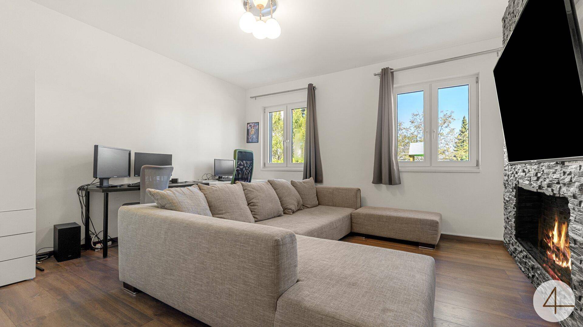 Gemütliches Wohnzimmer mit großem Sofa, Arbeitsbereich und modernem Kamin.
