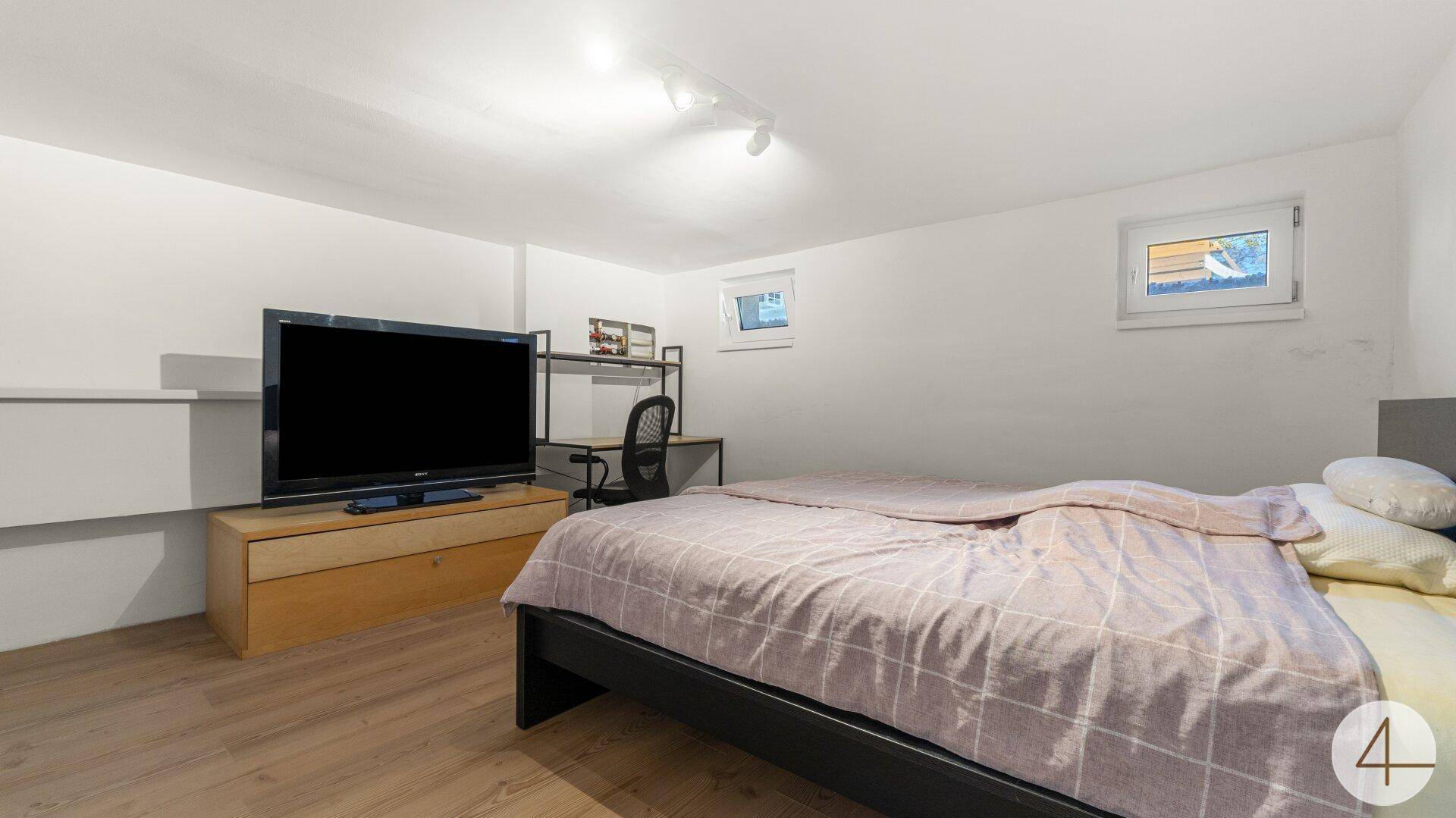 Geräumiges Schlafzimmer im Untergeschoss mit Fernseher, Schreibtisch und Bett.