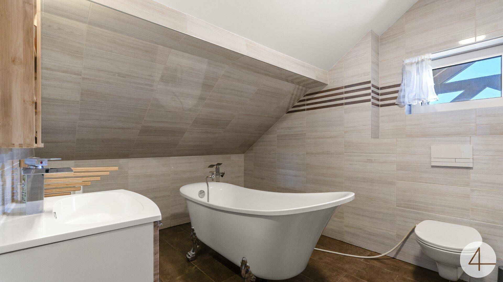 Helles Badezimmer im Dachgeschoss mit freistehender Badewanne, WC und Fenster.