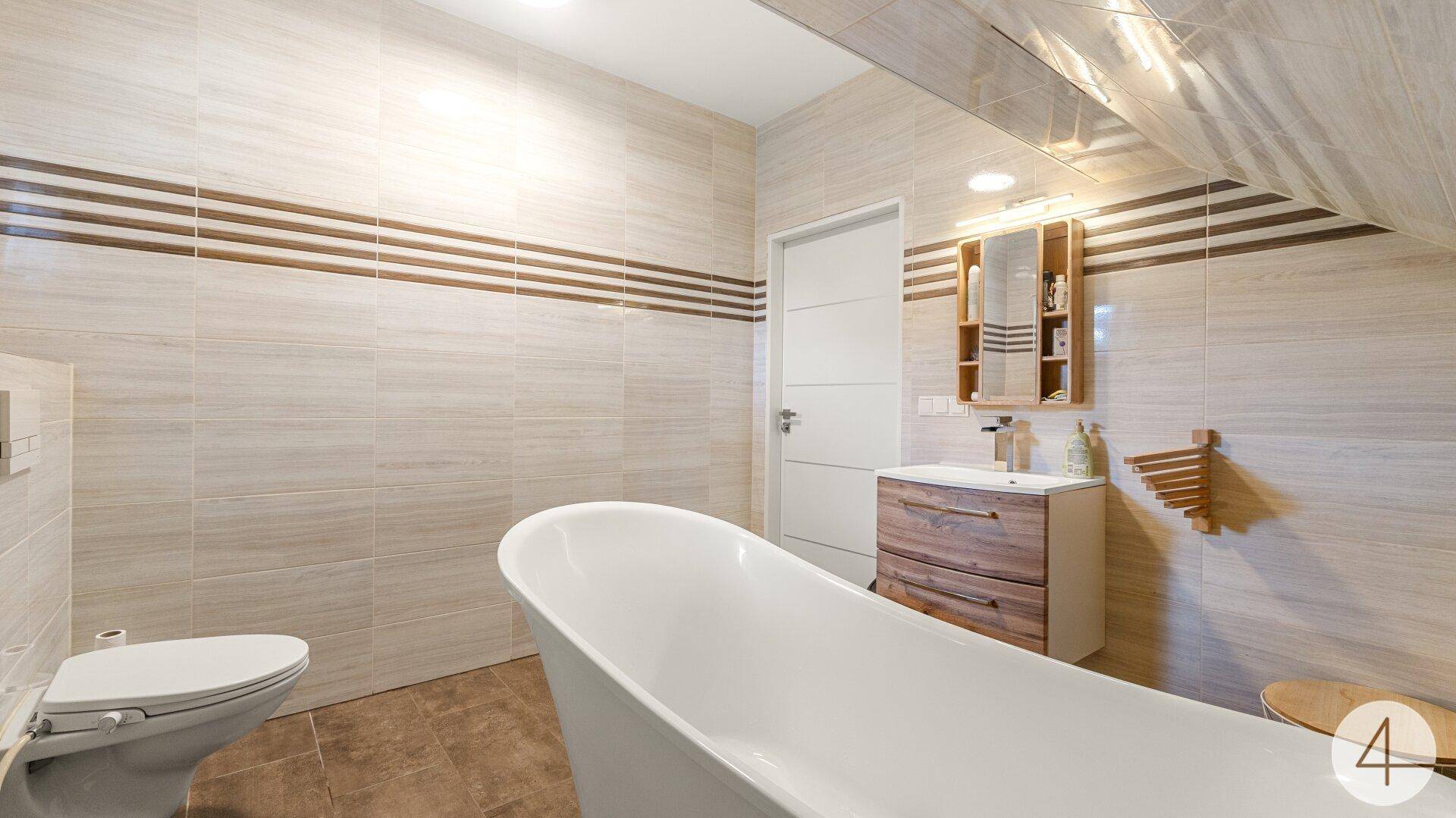 Helles Badezimmer im Dachgeschoss mit freistehender Badewanne und beigen Fliesen.