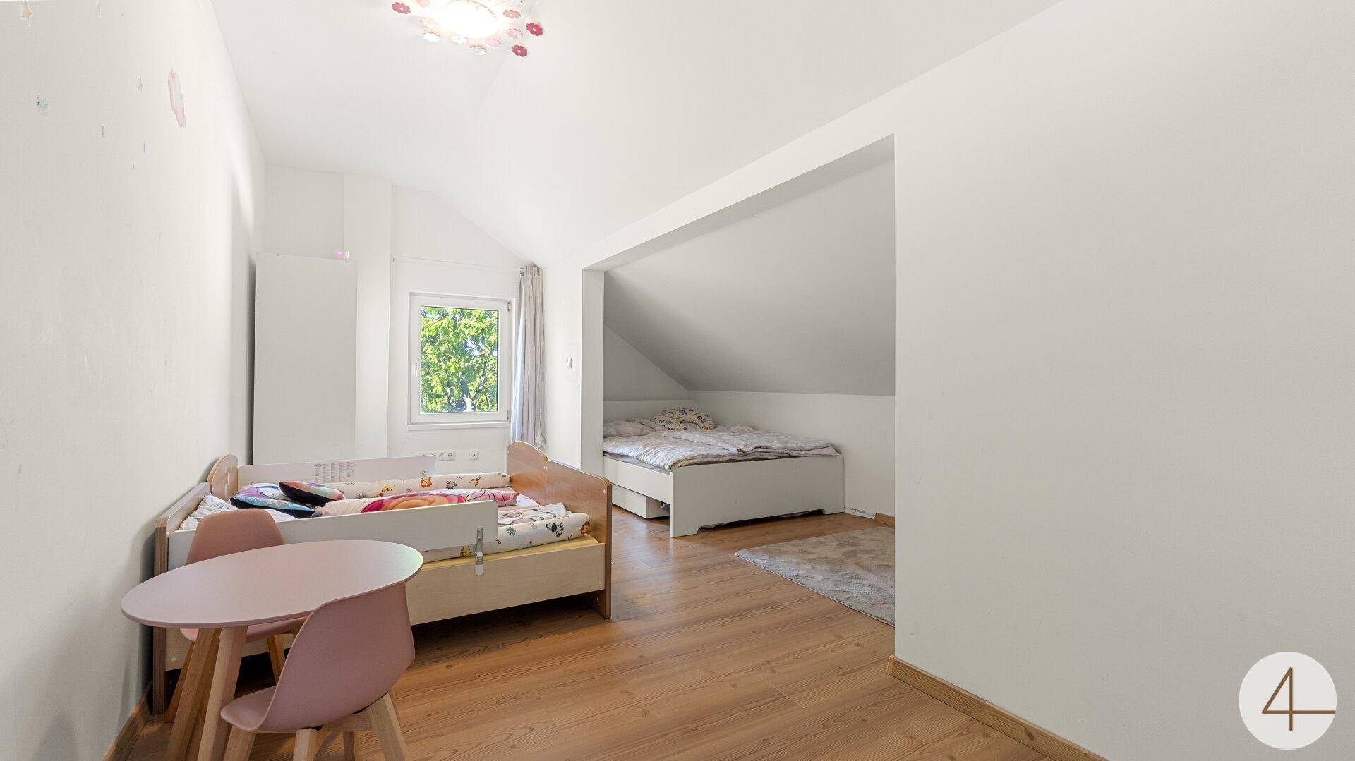 Kinderzimmer im Dachgeschoss mit schrägen Decken, Kinderbett und zusätzlichem Schlafbereich.