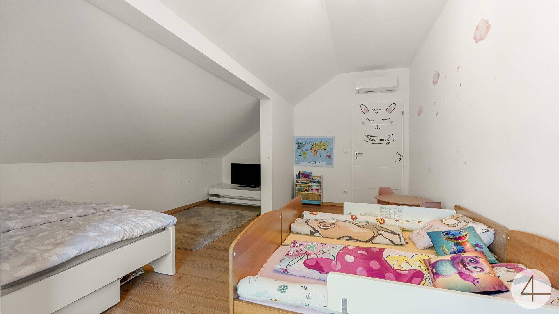 Kinderzimmer im Dachgeschoss mit zwei Betten, schrägen Wänden und Wanddekoration.