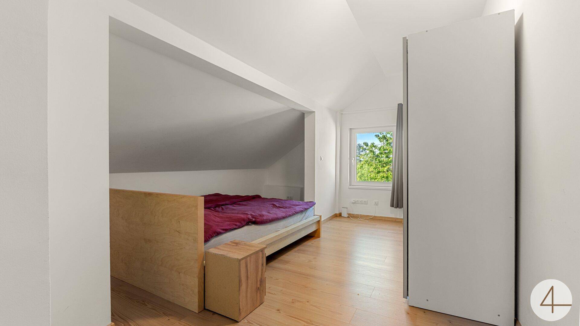 Schlafzimmer im Dachgeschoss mit Bett in einer Nische und Kleiderschrank.