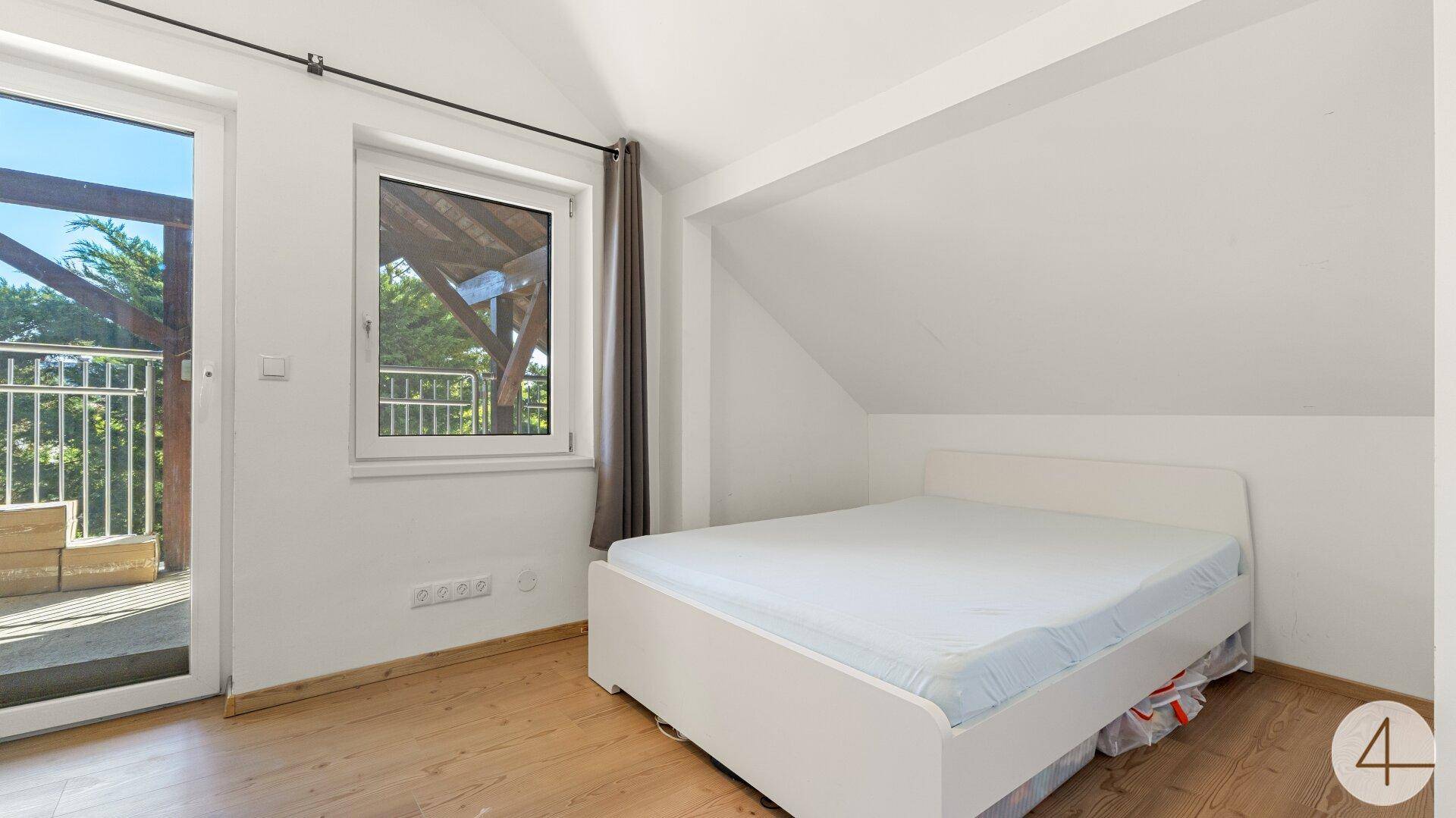 Schlafzimmer im Dachgeschoss mit Bett und Zugang zu einem Außenbereich.