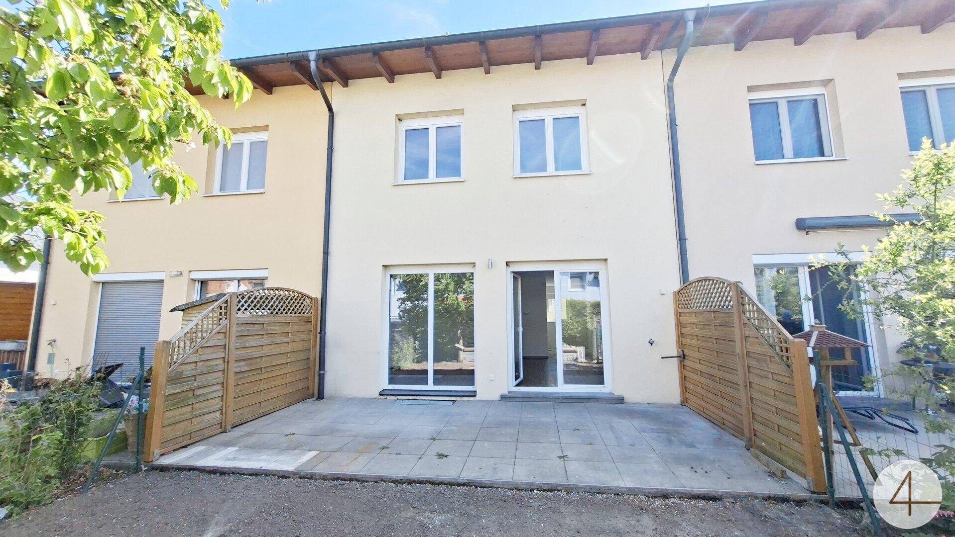 Rückseite eines Reihenhauses mit gepflasterter Terrasse und Zugang zum Gartenbereich.