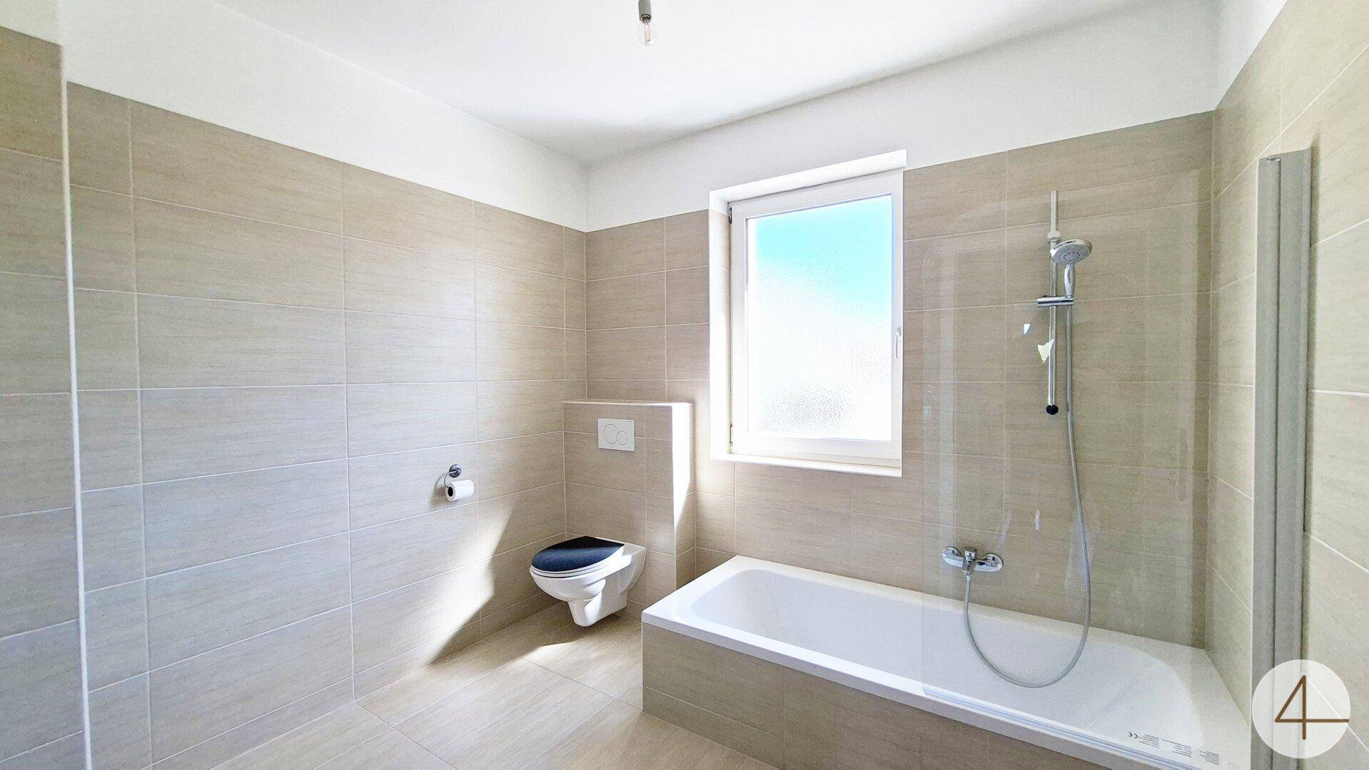 Modernes Badezimmer mit beigefarbenen Fliesen, Badewanne und Wand-WC.