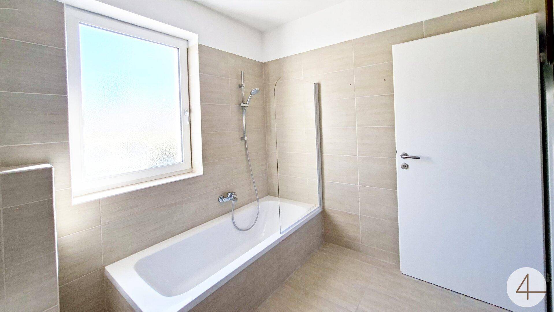 Helles Badezimmer mit Badewanne, Duschabtrennung und Fenster für Tageslicht.