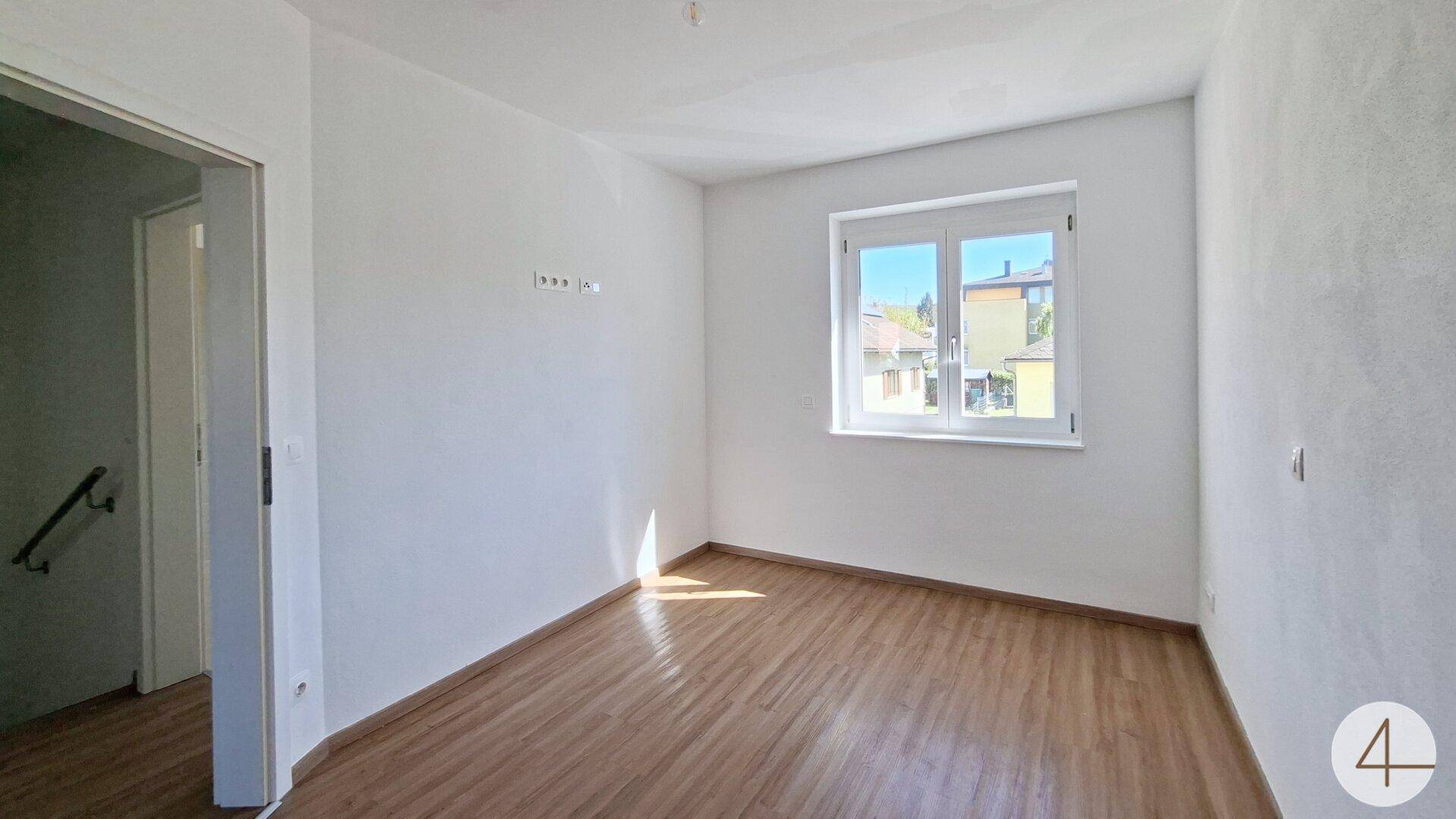 Helles Schlafzimmer mit Laminatboden und großem Fenster, bereit zur Einrichtung.