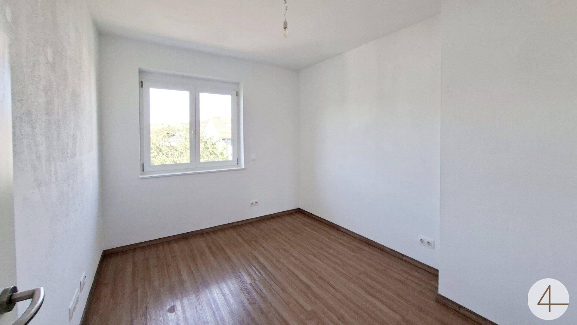 Lichtdurchflutetes Schlafzimmer mit Laminatboden und Blick ins Grüne.