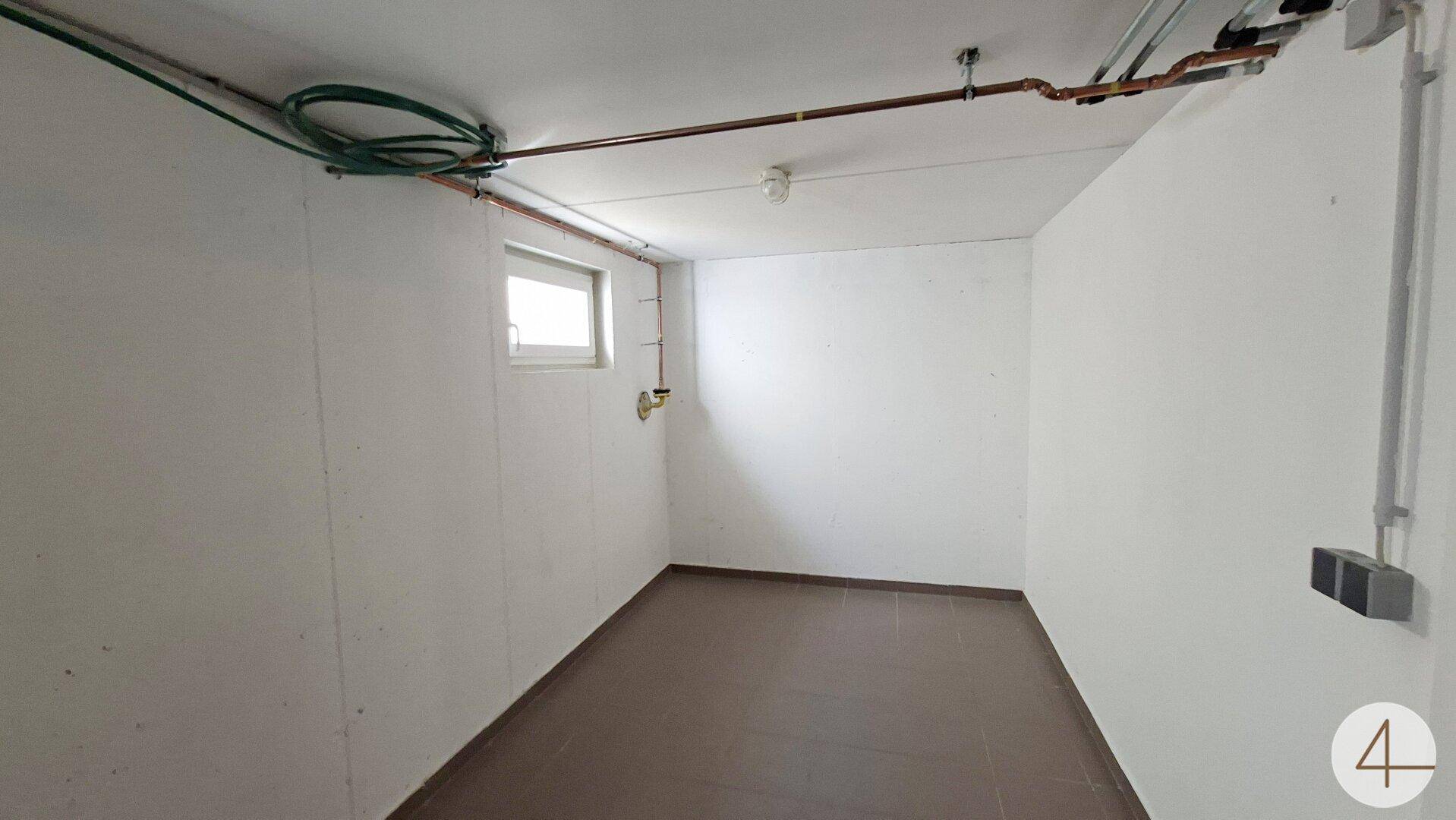 Einfacher Kellerraum mit Fenster, Fliesenboden und sichtbaren Installationen.