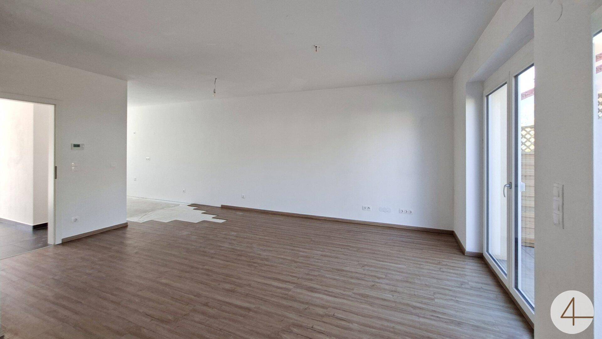 Lichtdurchflutetes Wohnzimmer mit Laminatboden und direktem Zugang zur Terrasse.